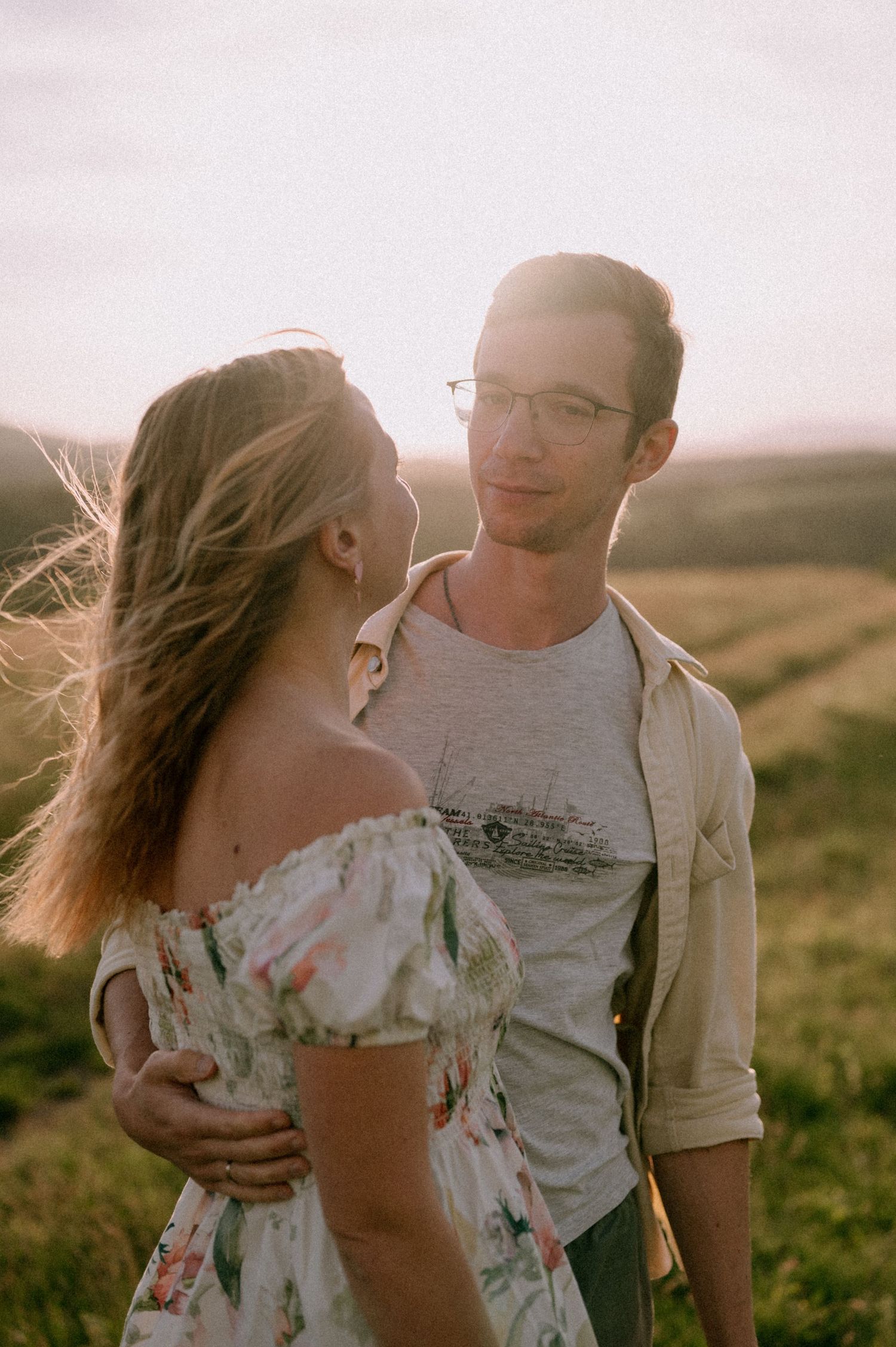 Tender moment between couple in casual attire against mountain backdrop at dusk.