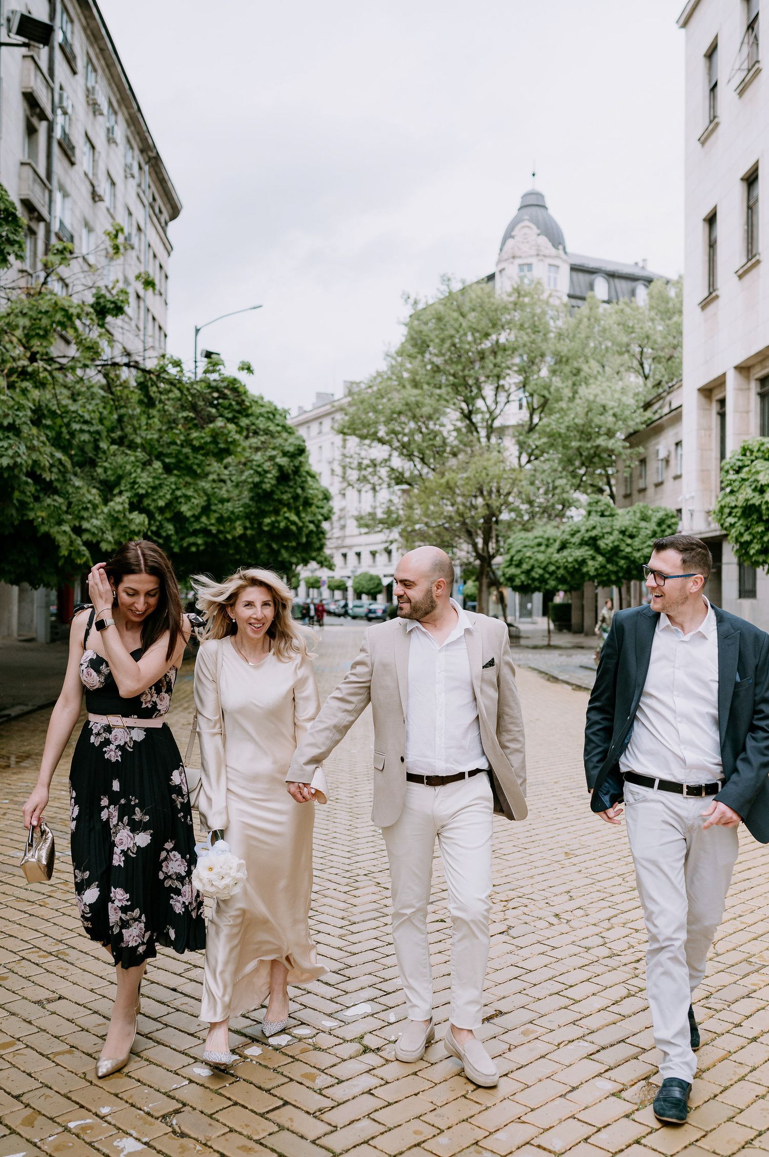 Friends walking and holding hands along a European street lined with historic buildings.