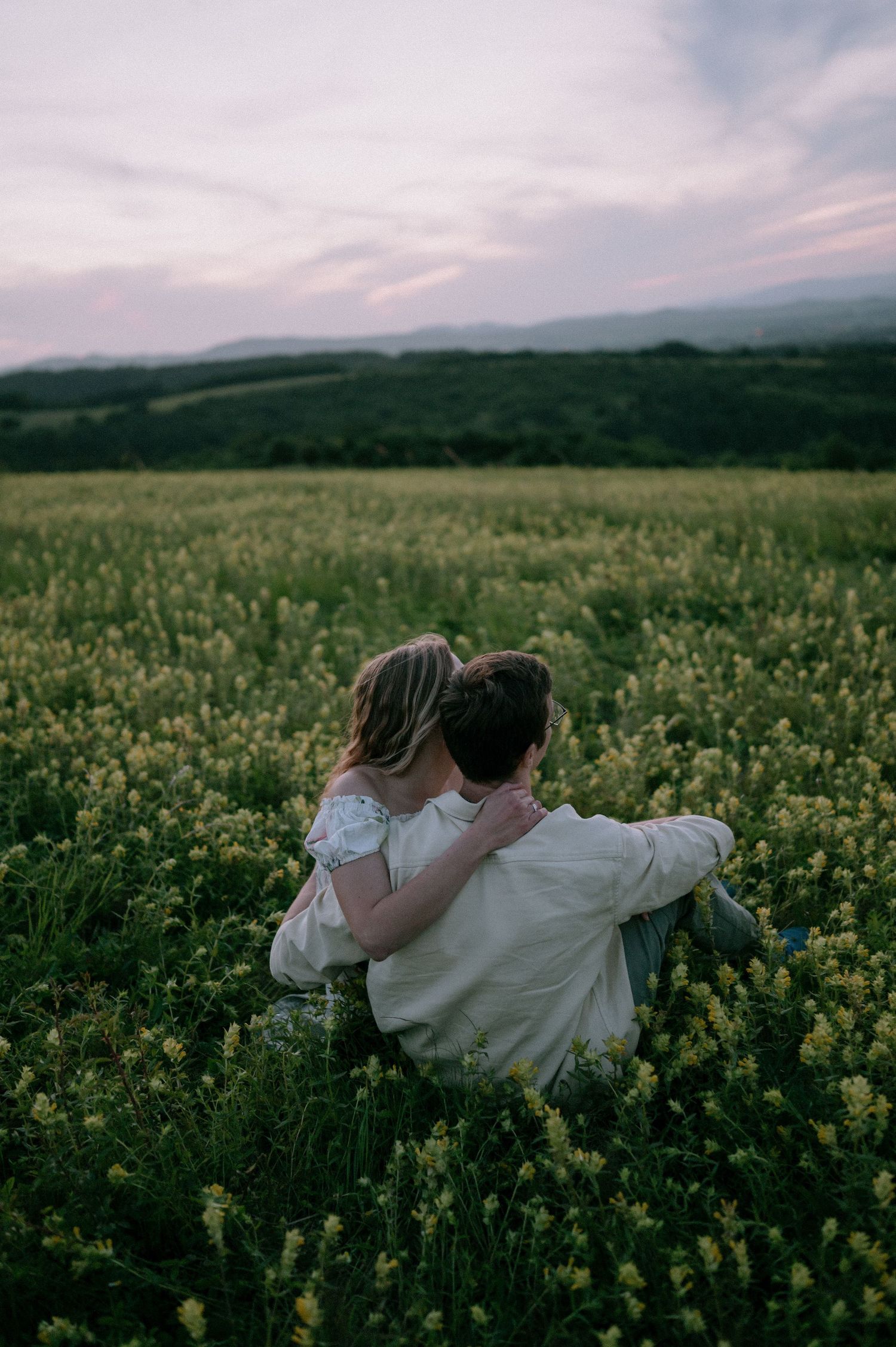 A couple snuggles close together in a scenic yellow flower field at sunset.