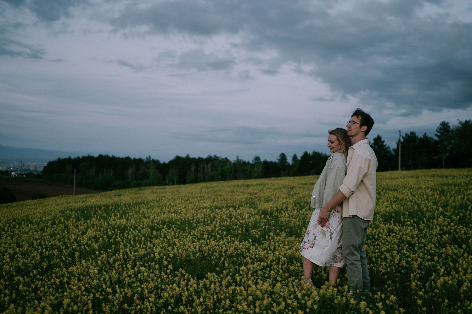 A romantic photoshoot in a vast yellow flower field under moody skies.