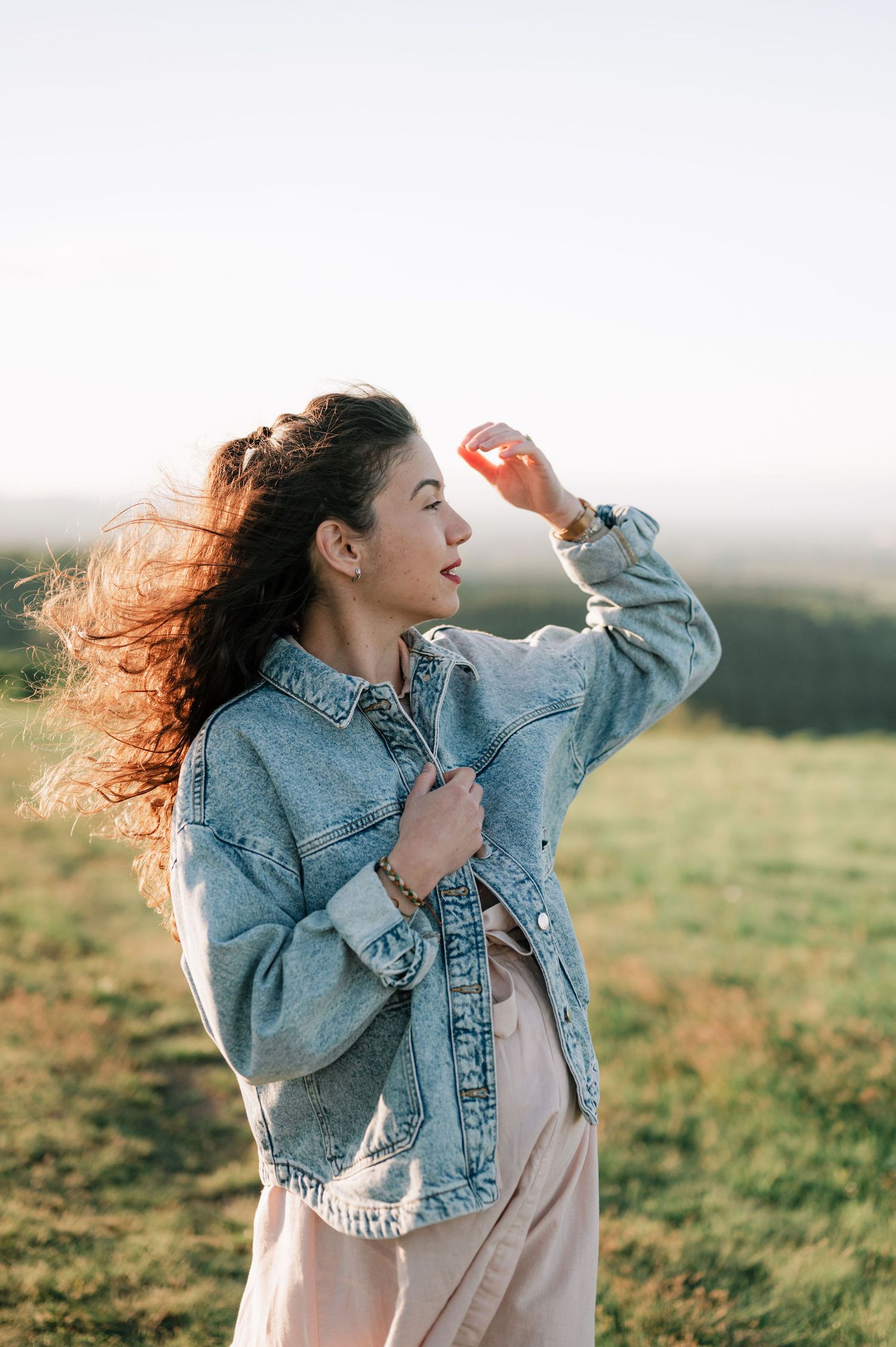Woman in denim jacket stands in sunlit field with windswept hair in artistic photo series.