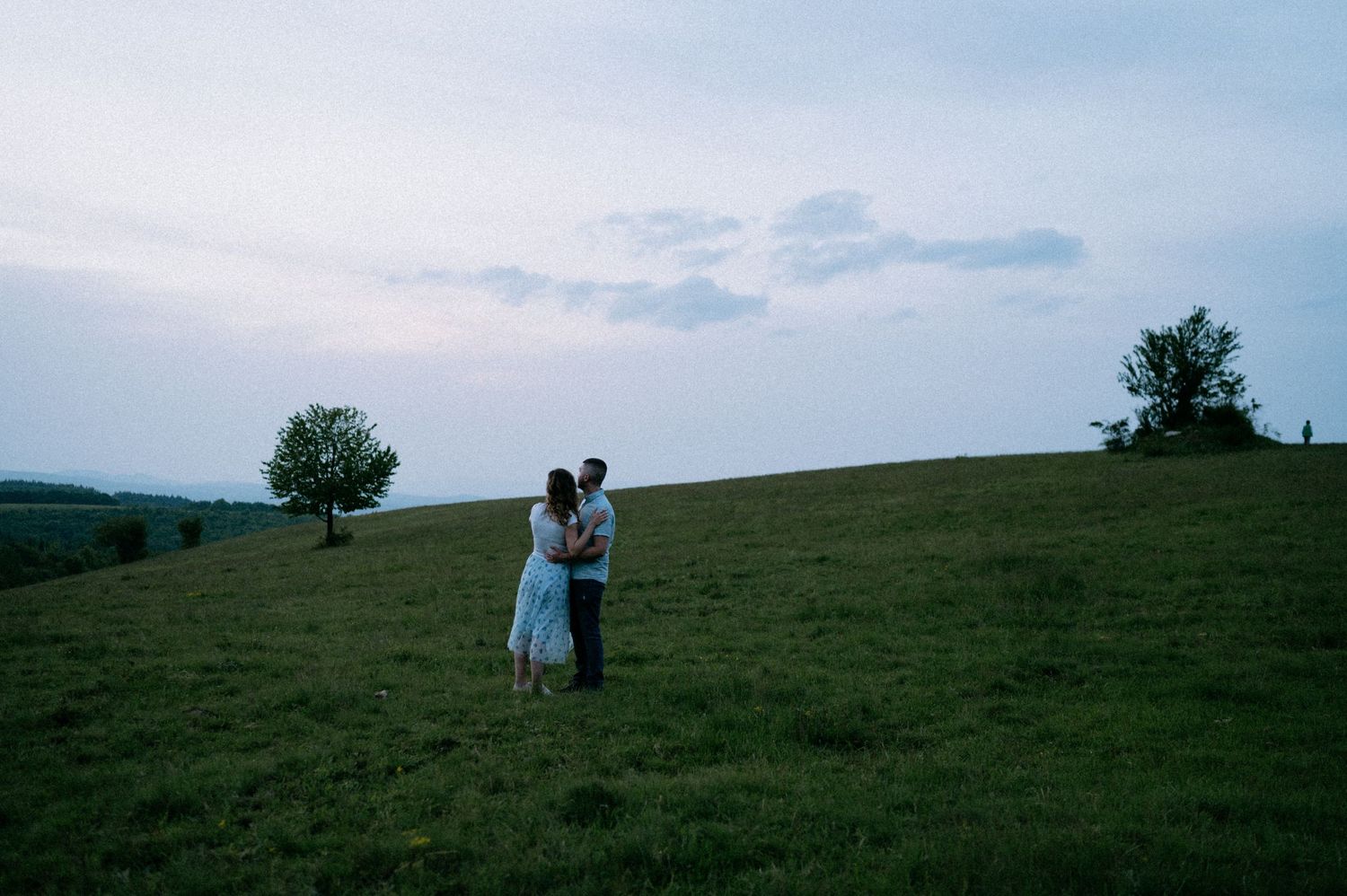 A couple embraces on a grassy hilltop at sunset.