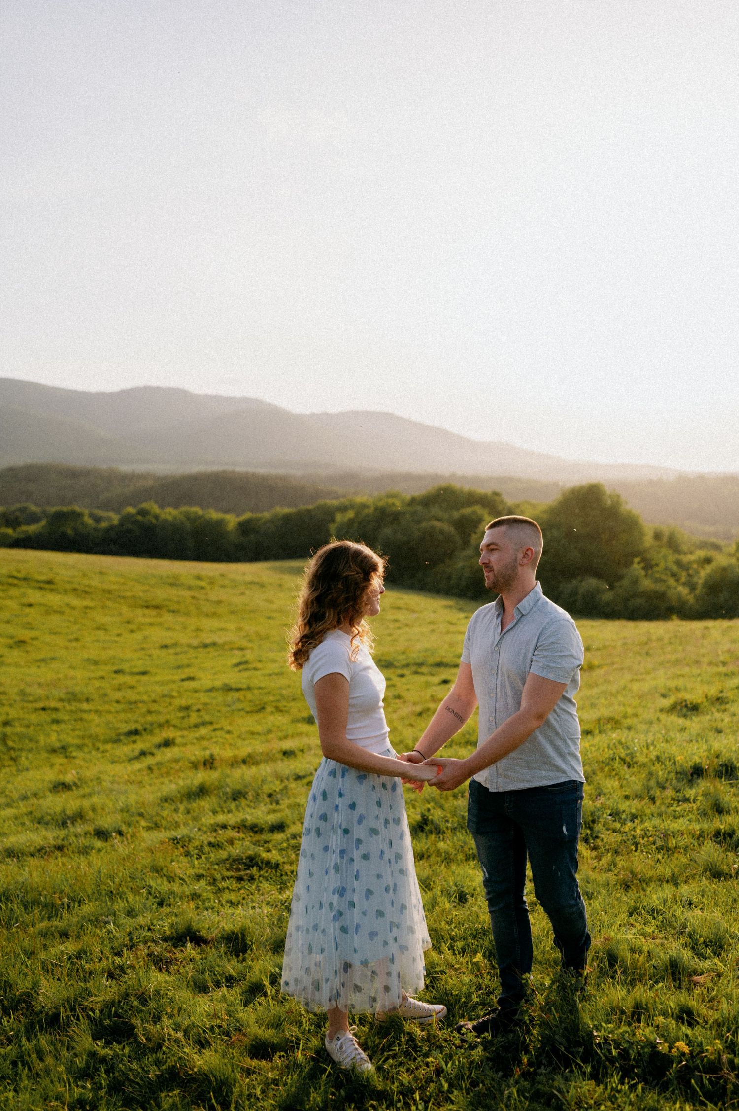 Two people dance and twirl together on a hilltop meadow during a warm summer evening.