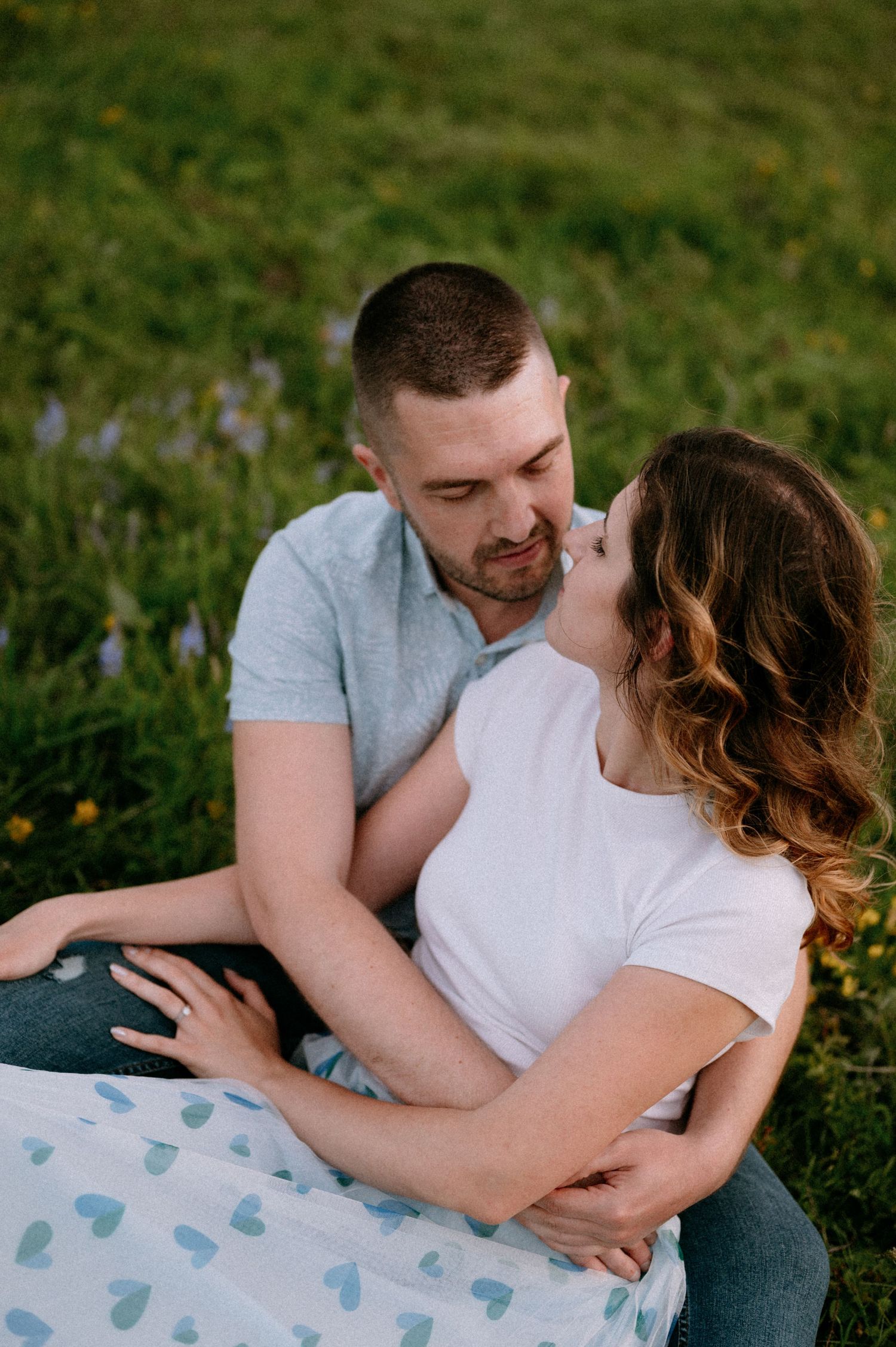 Close-up of couple sharing tender moment on blanket in flowering mountain meadow.
