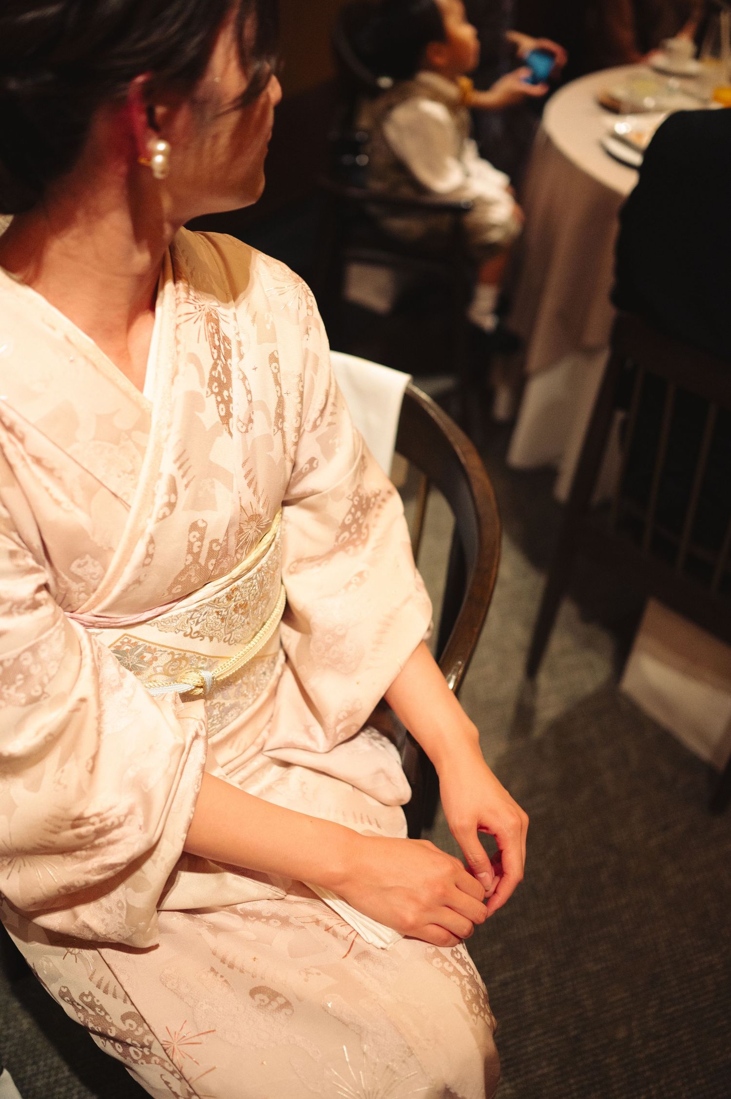 Person wearing delicate white silk kimono sits during formal celebration.