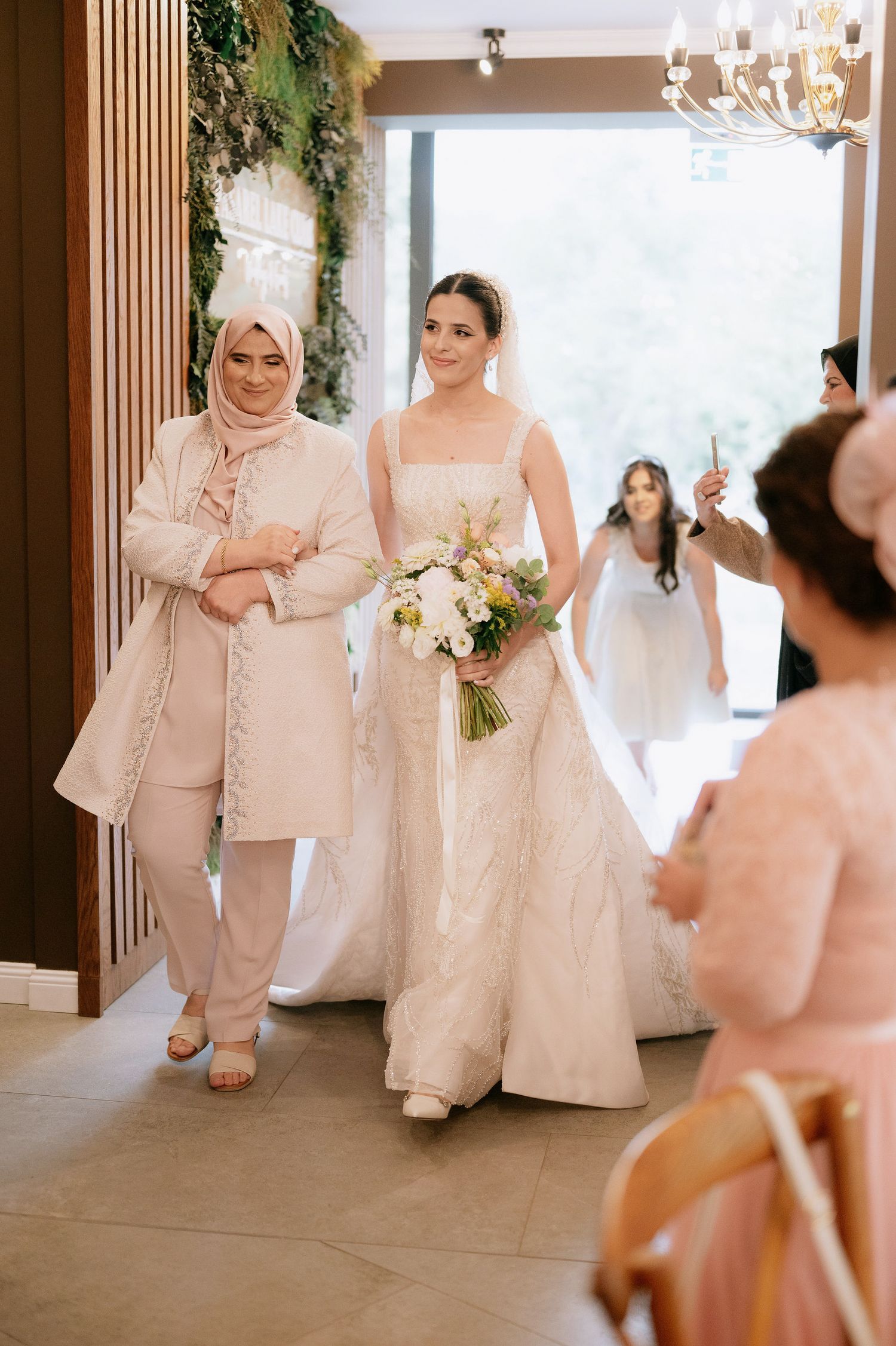 Wedding party members in cream and white formal attire walk through an elegant venue.