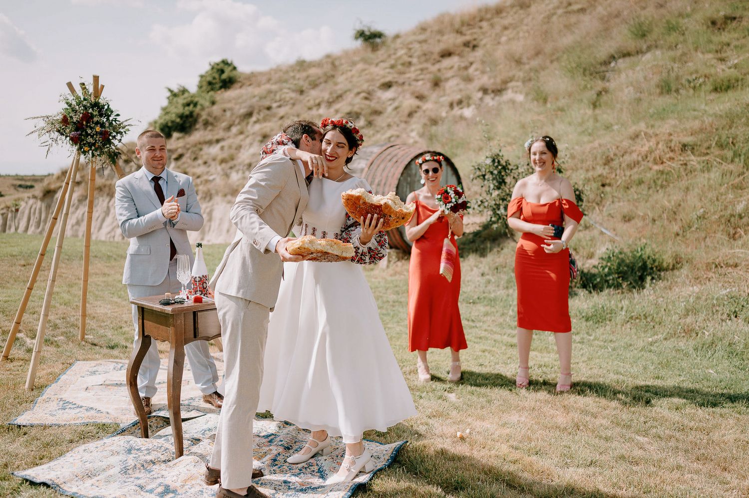 Panoramic view of an outdoor wedding ceremony with red bridesmaids and wooden arch decorations.