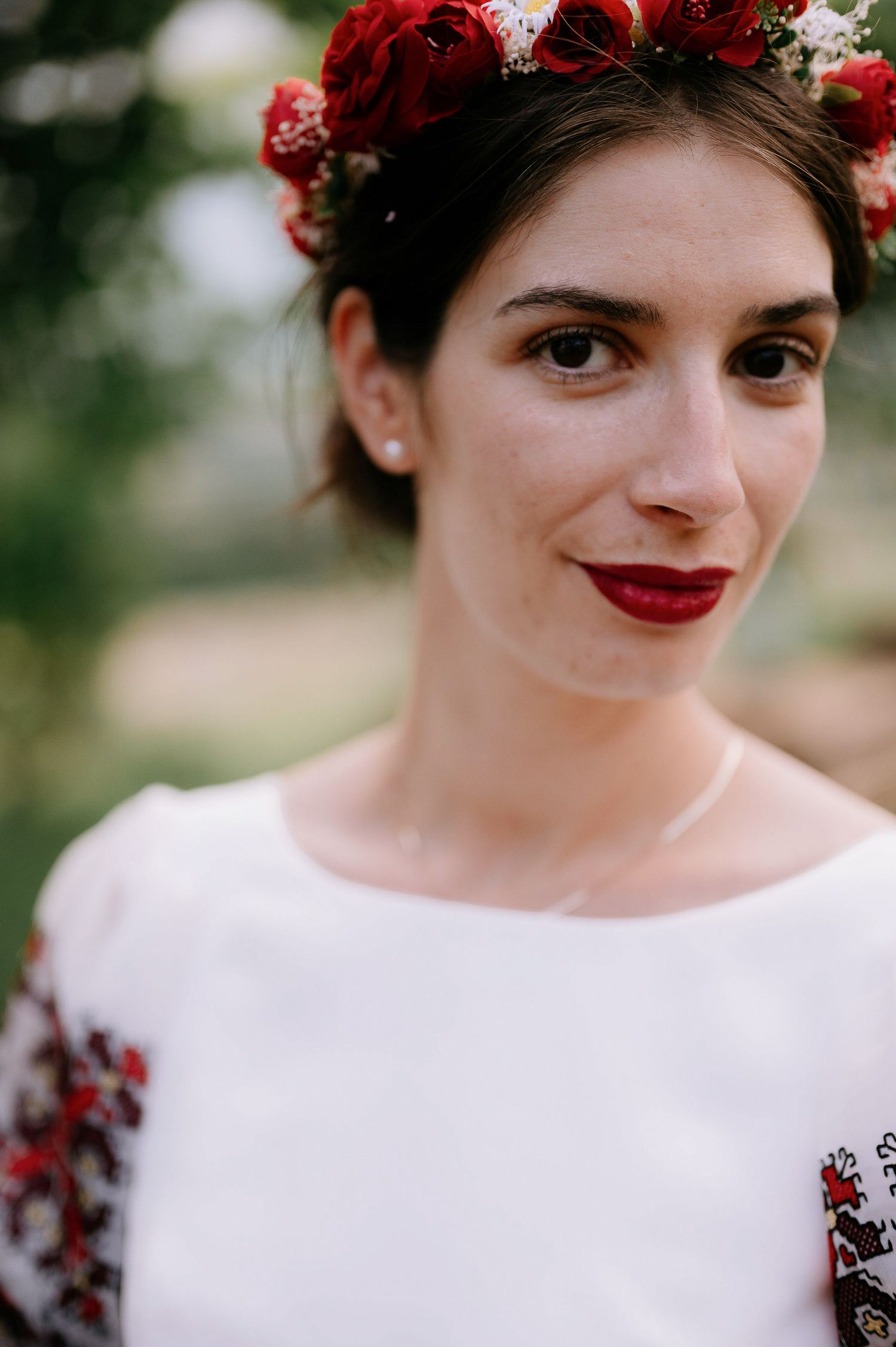 Close-up shots highlighting red floral crown and white dress with embroidered details.
