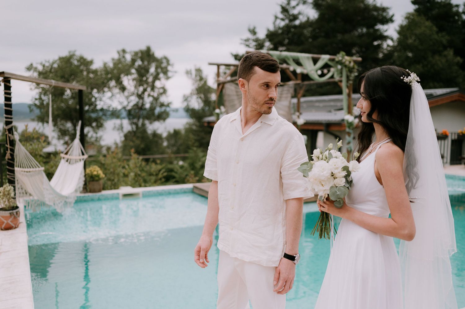 Wedding couple shares intimate moments by a poolside with mountain scenery in the background.