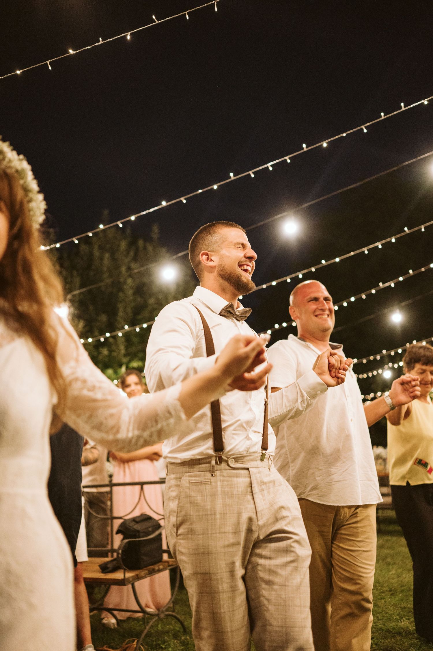 Wedding party celebrates with dancing under string lights at outdoor reception.