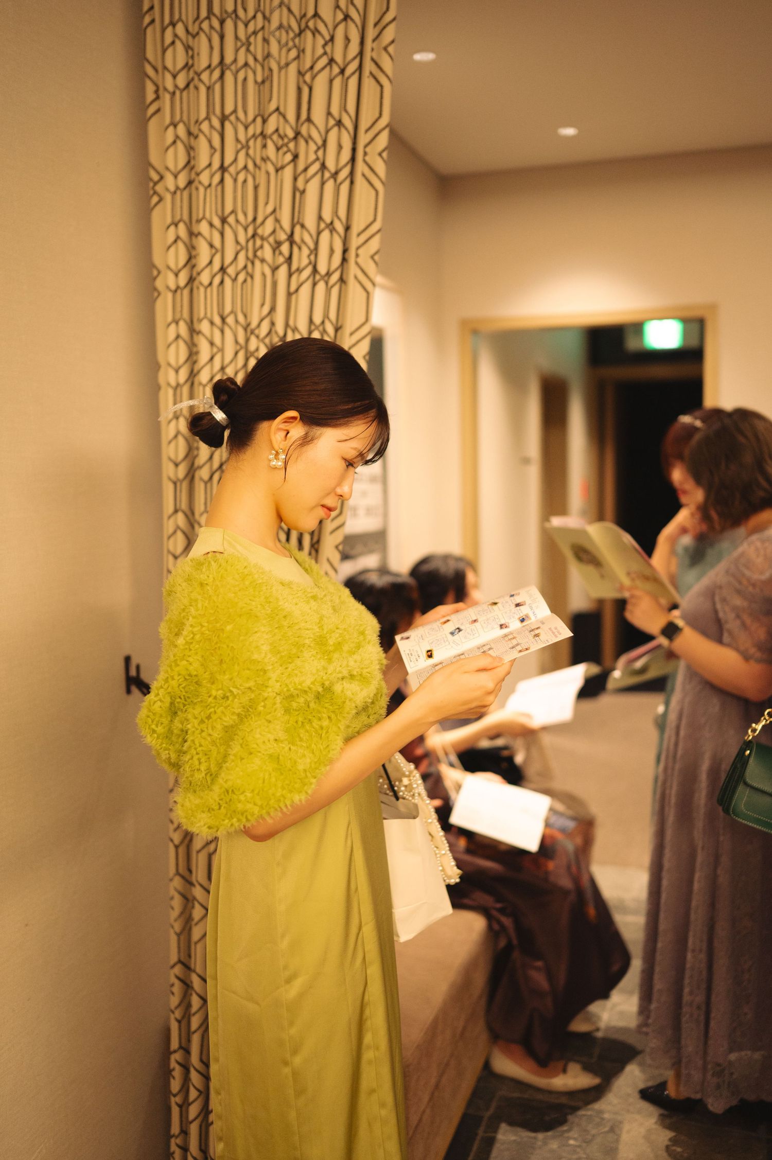 Wedding attendees in formal attire reviewing programs in a hotel hallway.