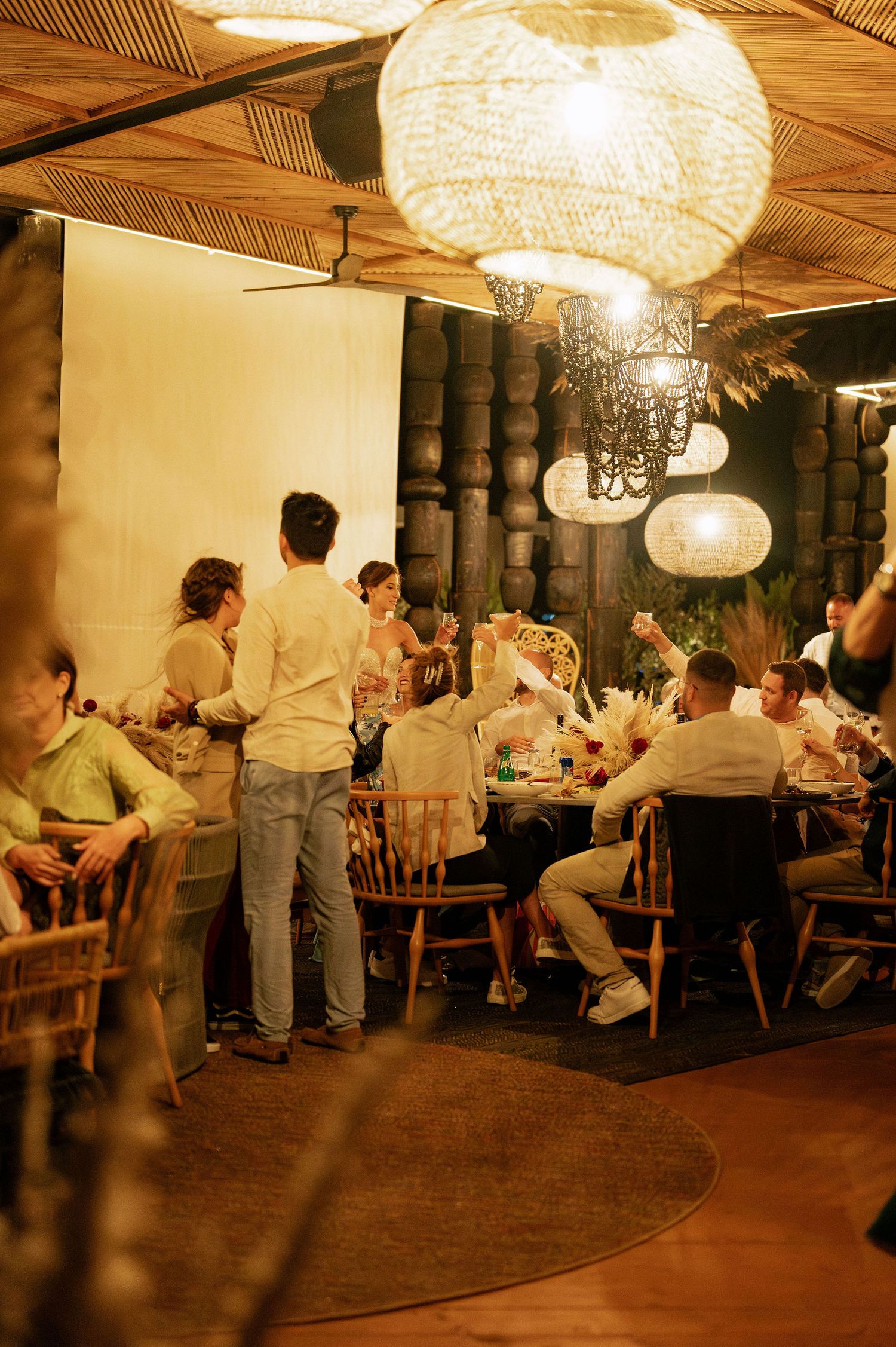 Wedding reception venue with large pendant lights and guests seated at long tables.