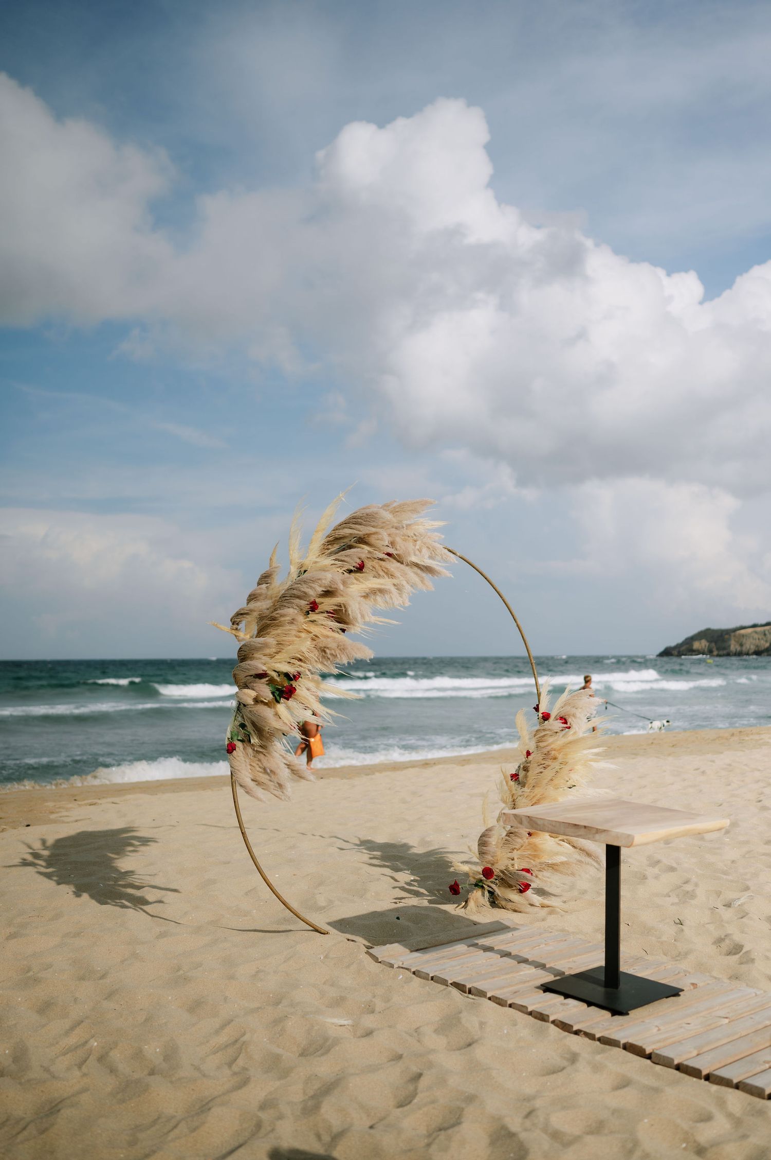 Dried pampas grass wedding arch installation on a windy beach.