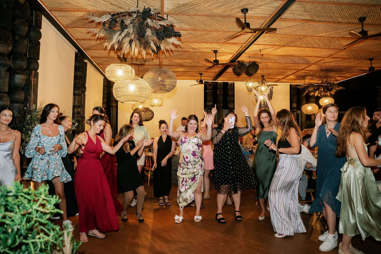 Wedding guests dancing and celebrating in a rustic venue with wooden ceiling details.