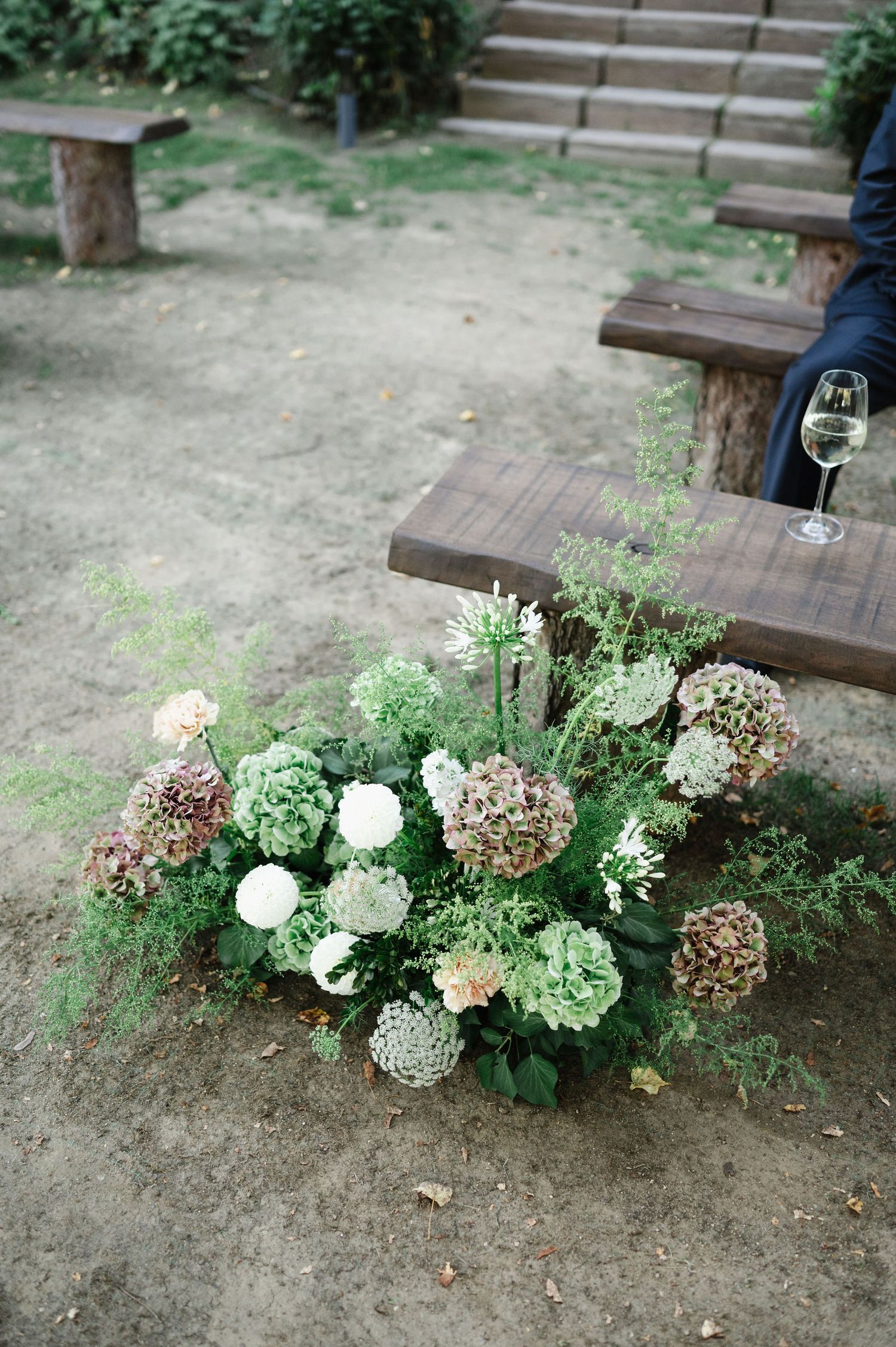 White and green floral arrangements decorating wooden bench seating area.