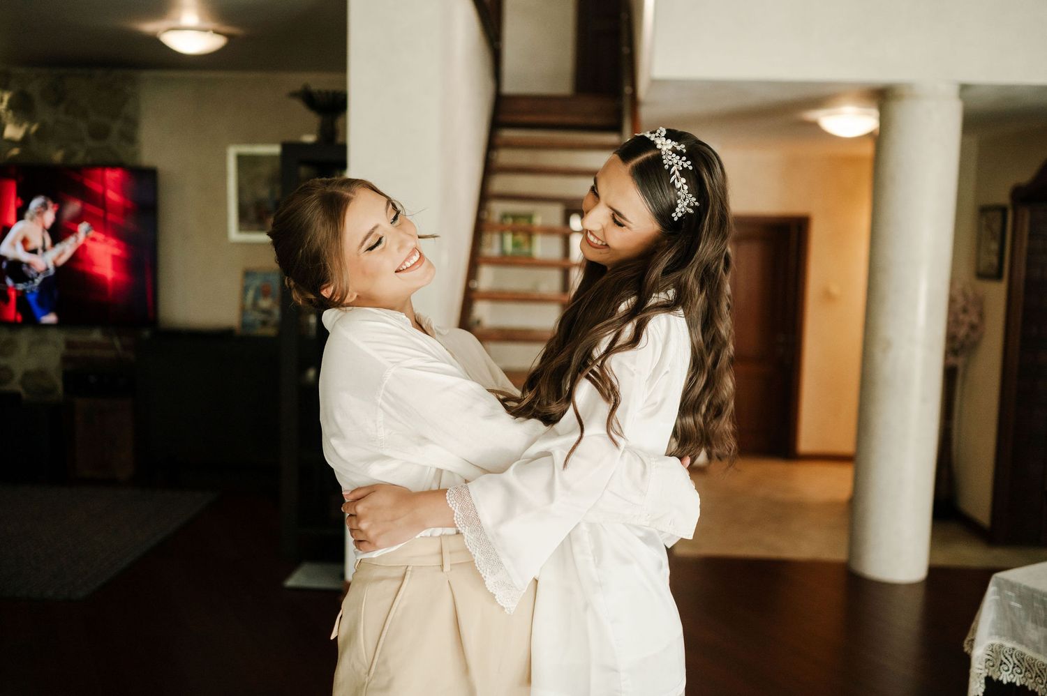 Two women in white robes share a joyful moment together while getting ready.