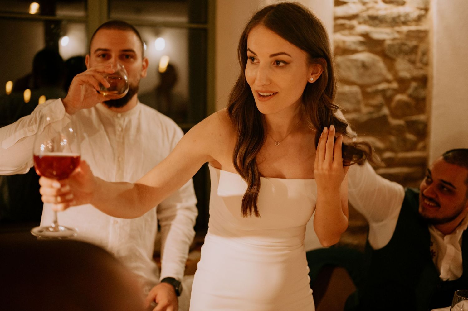 Joyful wedding reception scene with guests dining and socializing in a warmly lit stone interior.