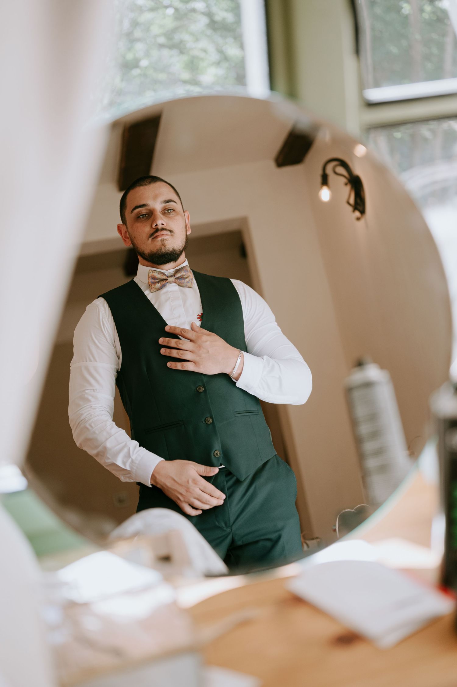 A person in formal attire adjusts their outfit near a bright window.
