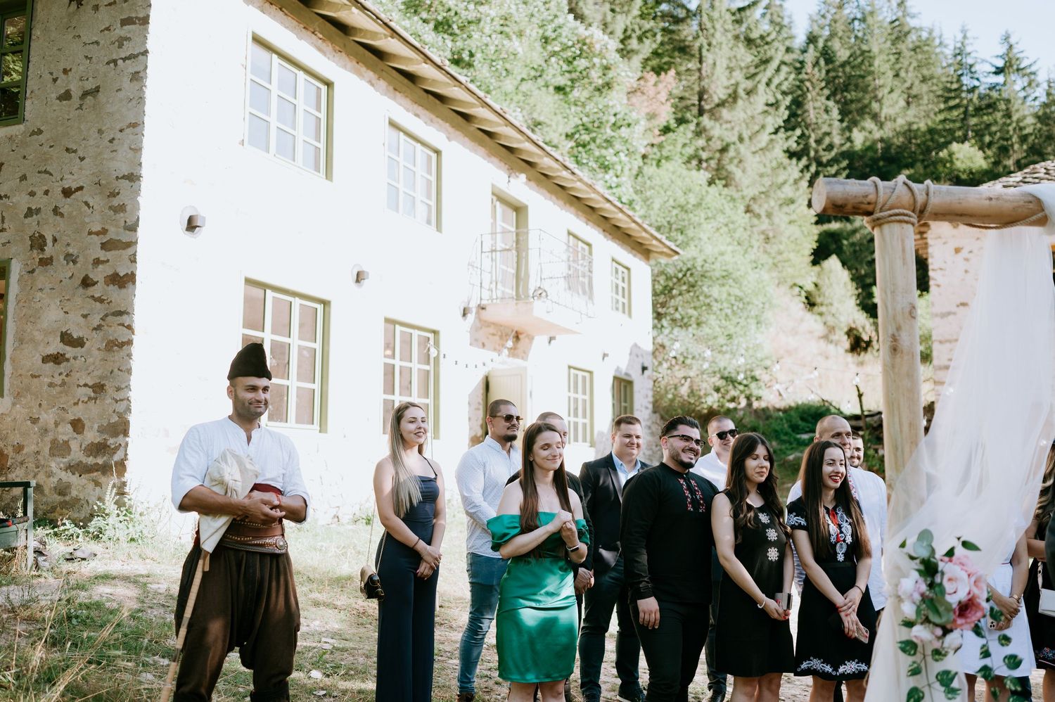 Guests mingle during outdoor wedding reception near rustic stone building.
