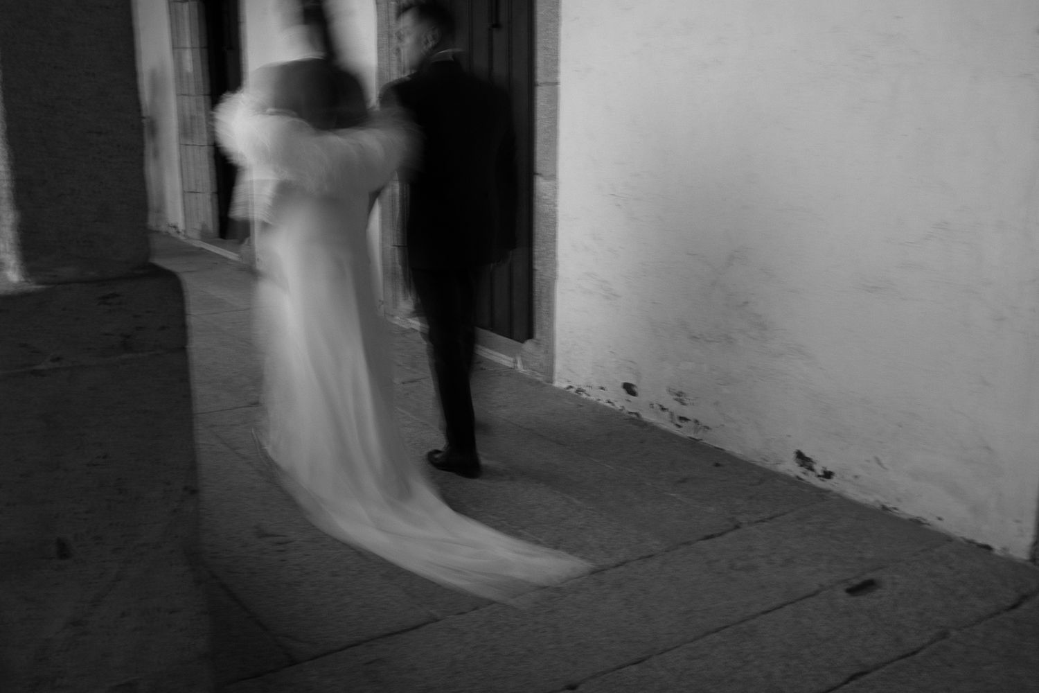 Ethereal black and white wedding photo with motion blur in a hallway.