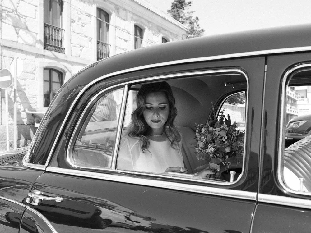 Novia sentada en un coche antiguo, fotografía en blanco y negro con aire clásico y atemporal.