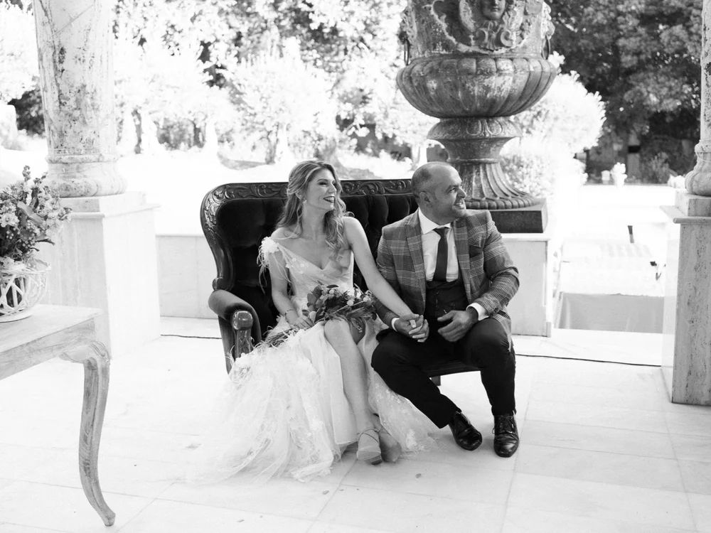 Pareja de novios sentados en un sofá de estilo vintage durante su ceremonia de boda, fotografía en blanco y negro.