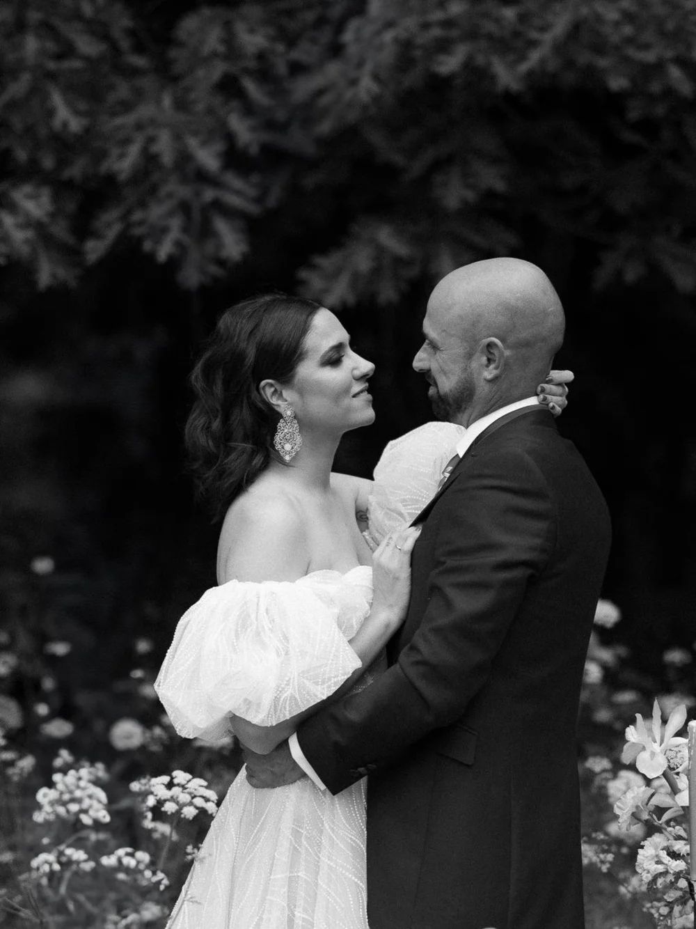 Pareja de novios en un jardín con flores blancas, momentos íntimos en blanco y negro llenos de emoción.