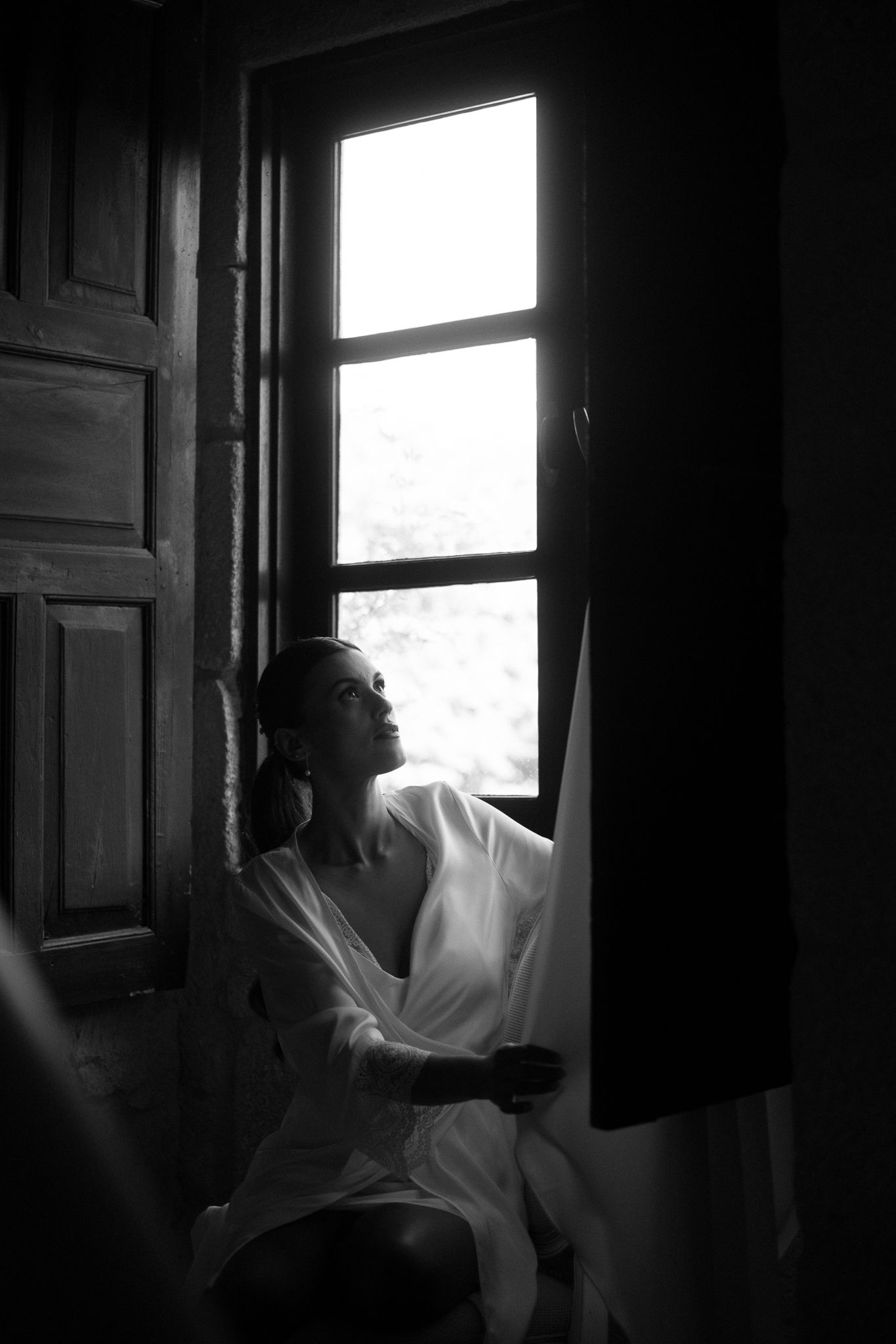 Black and white photo of a silhouetted figure gazing through an open window in a dark room.