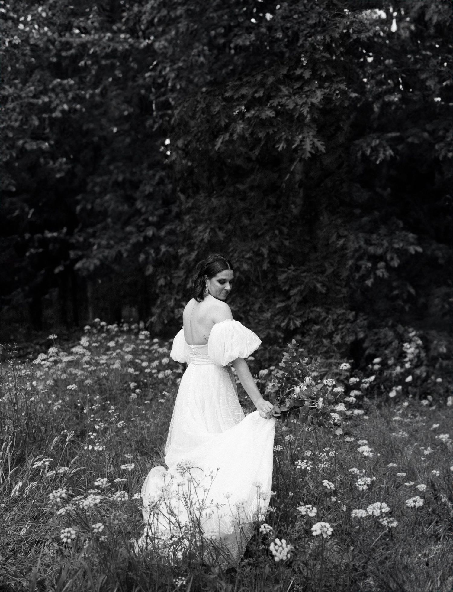 White wedding dress flowing through a meadow of wildflowers in natural light.