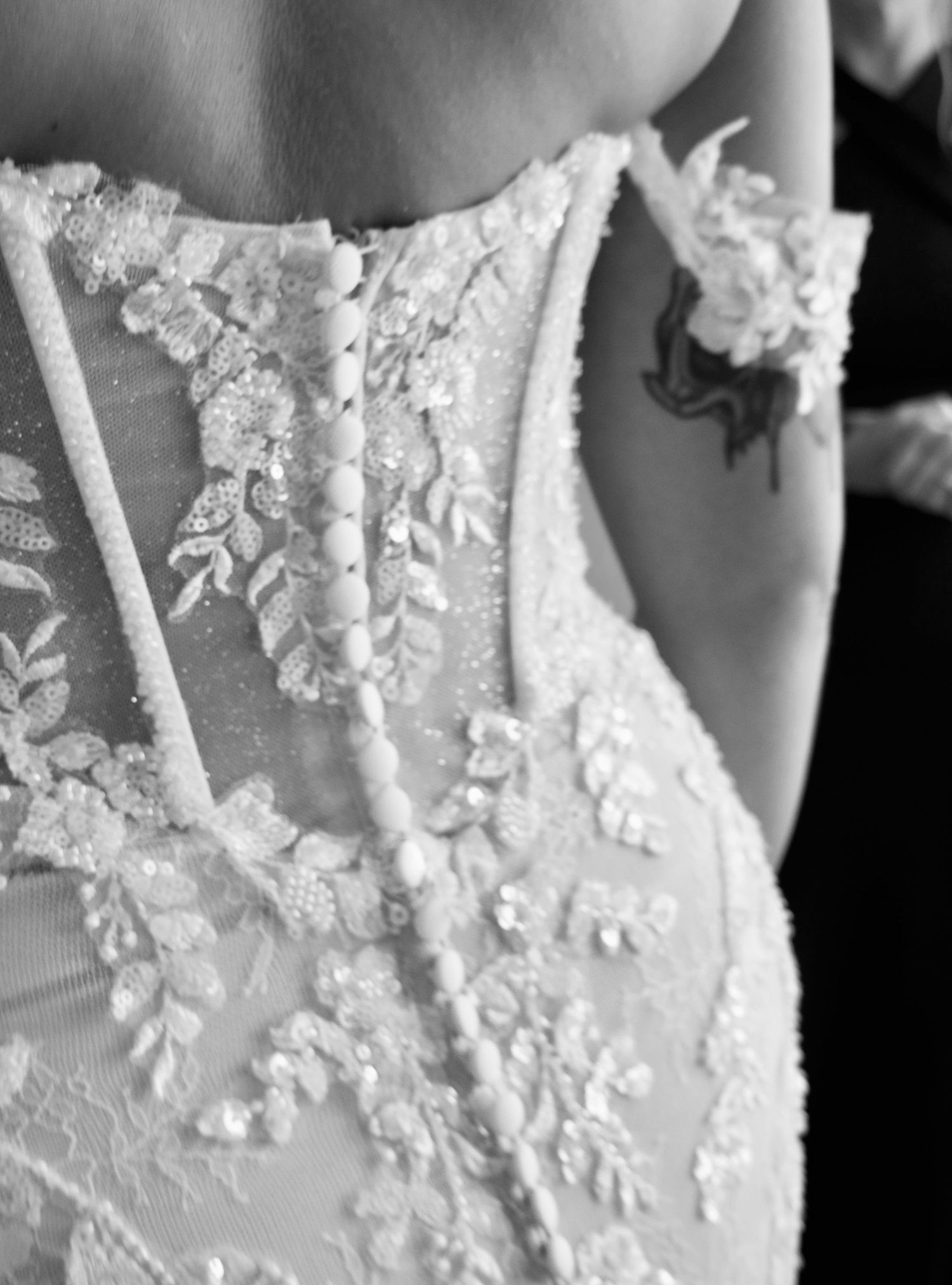 Close-up black and white detail of intricate lace and pearl button wedding dress corset back.