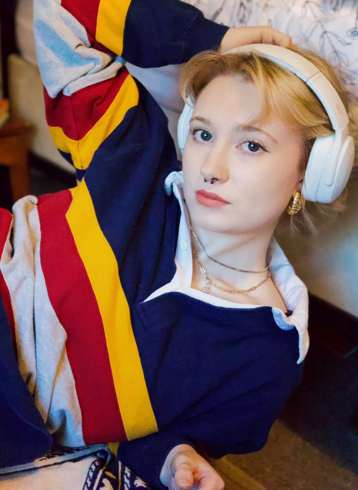 Young person with blonde hair wearing white headphones and a colorful striped jacket, posing casually.