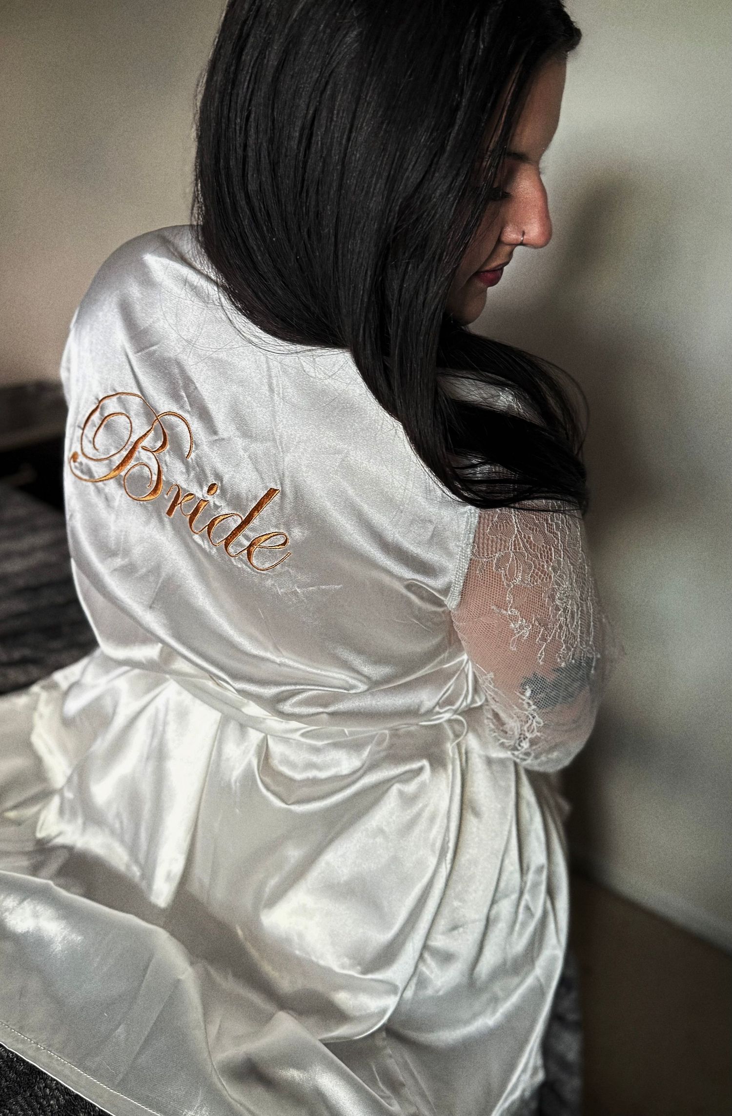 Woman wearing a white satin bridal robe with gold embroidered Bride script and lace sleeves.