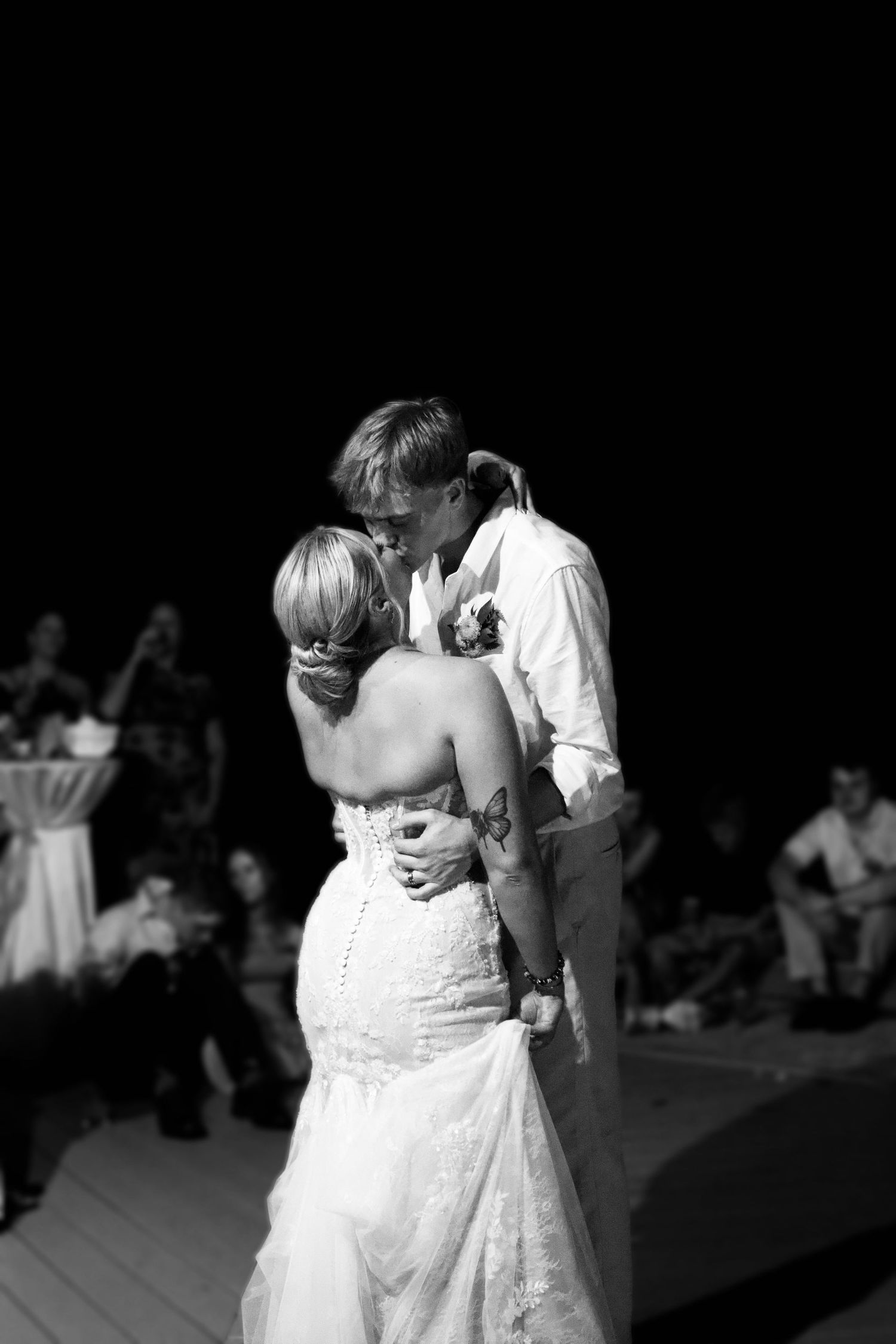Black and white photo of a bride and groom sharing their first dance kiss at a wedding reception.