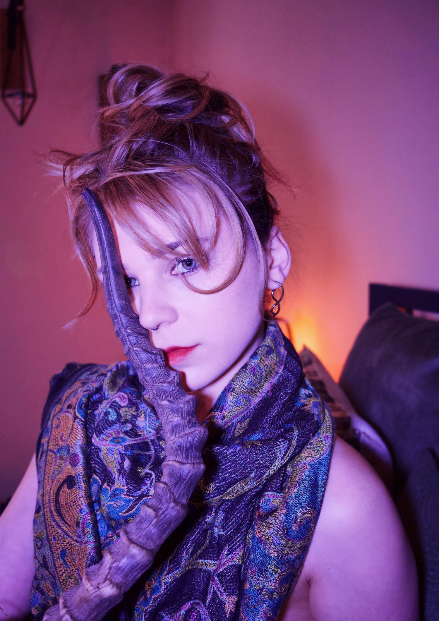Woman with updo hairstyle wearing a colorful paisley scarf, posing under purple and pink lighting.