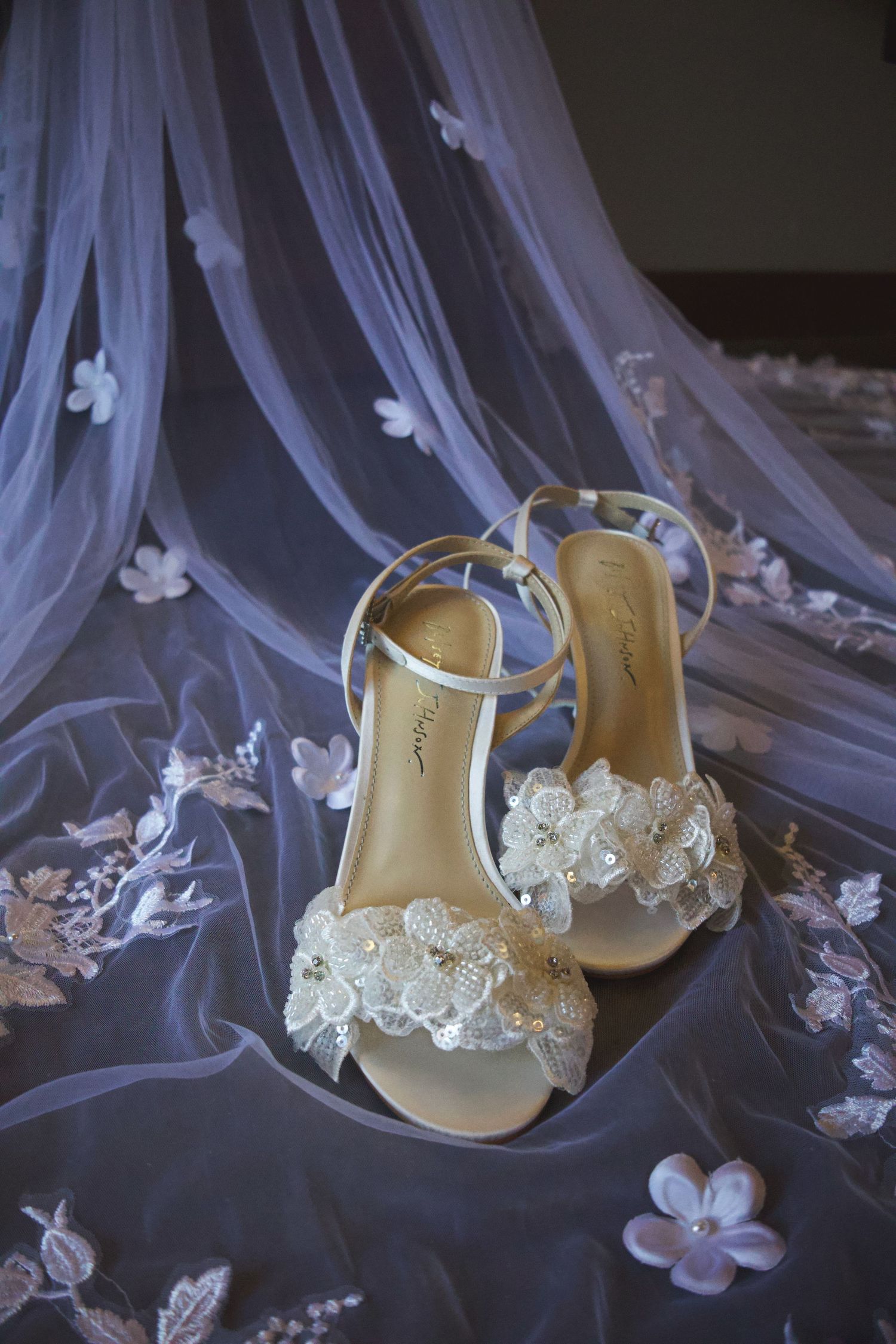 Elegant bridal heels with floral lace embellishments resting on a delicate embroidered wedding veil.