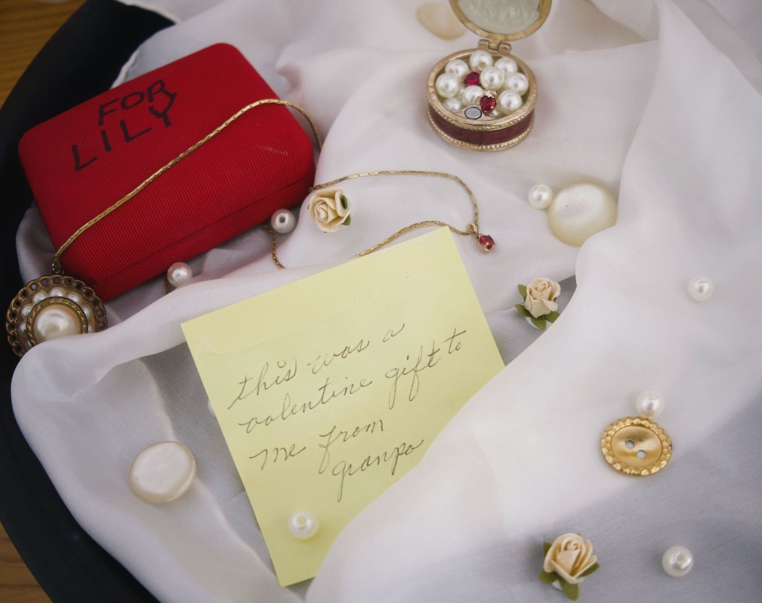 Vintage jewelry collection with pearl accessories, gold rose pins, a red velvet box labeled Lily, and a handwritten Valentine's note.