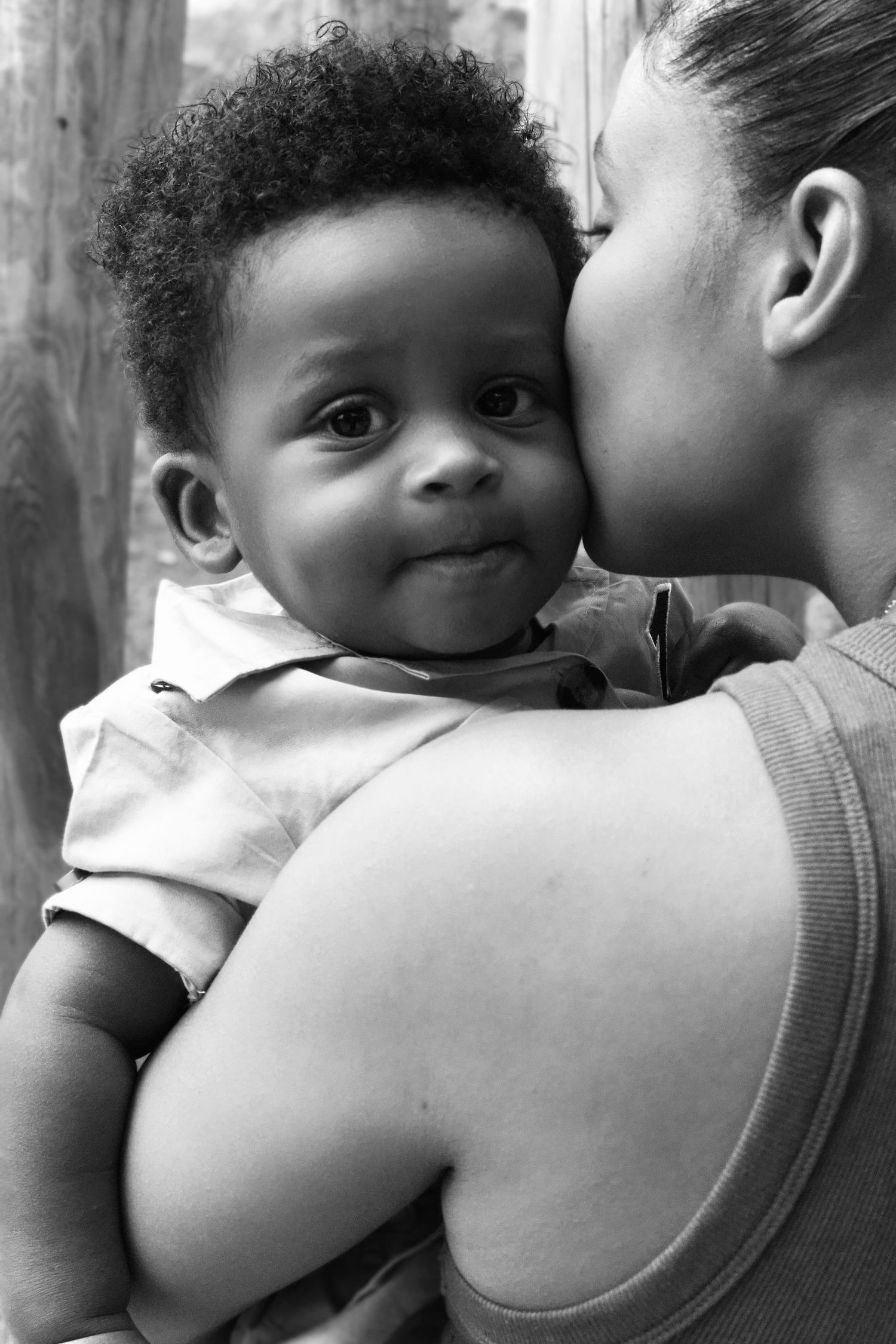 Black and white photo of a mother kissing her smiling baby boy on the cheek while holding him tenderly.