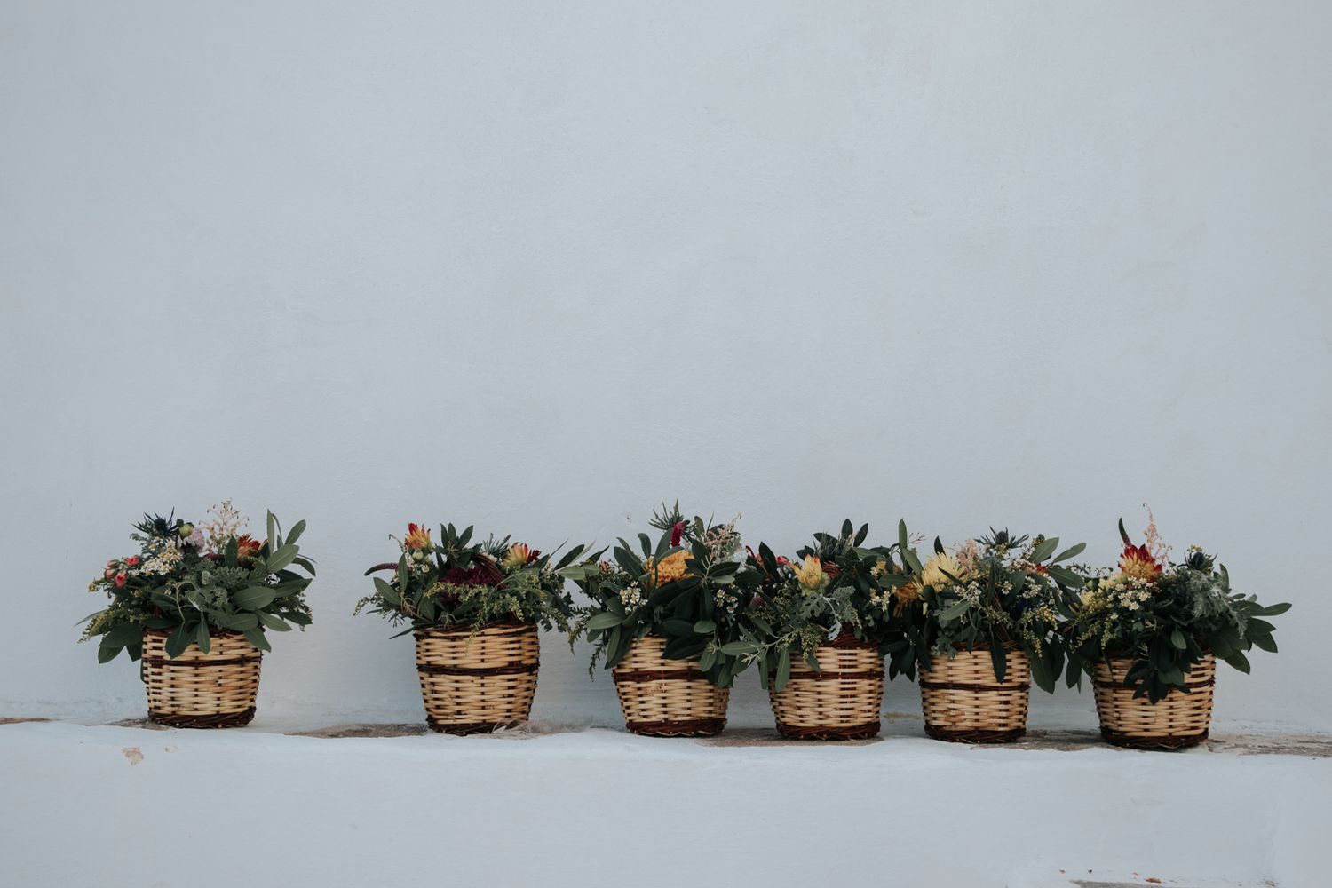 Row of wooden barrel planters with flowers arranged against a white wall.