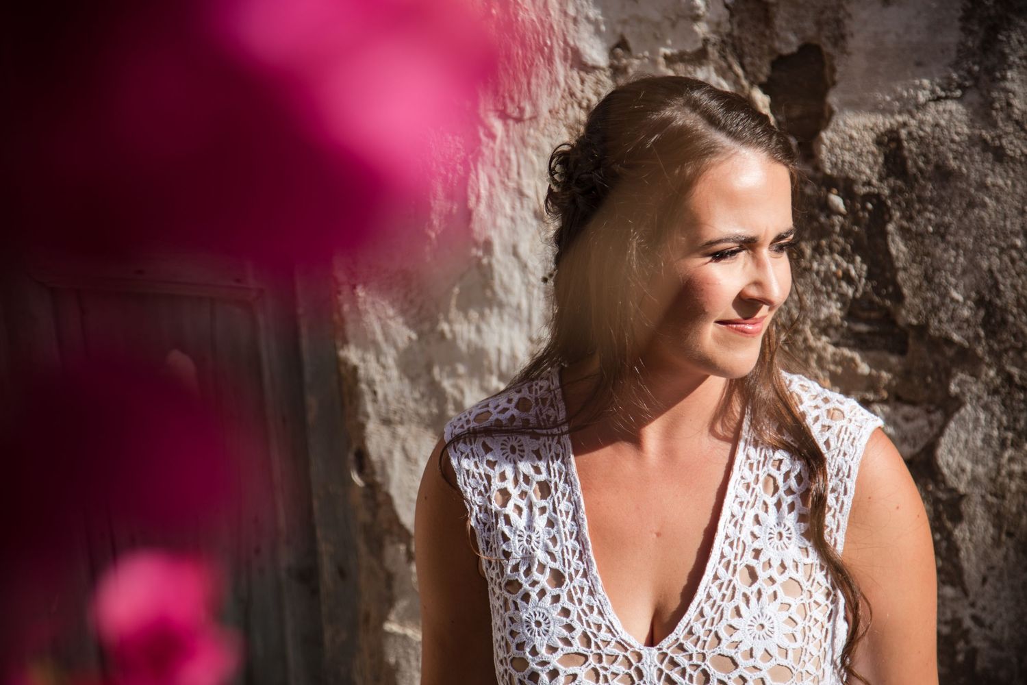 Romantic portrait session against a stone wall with pink floral elements in soft lighting.