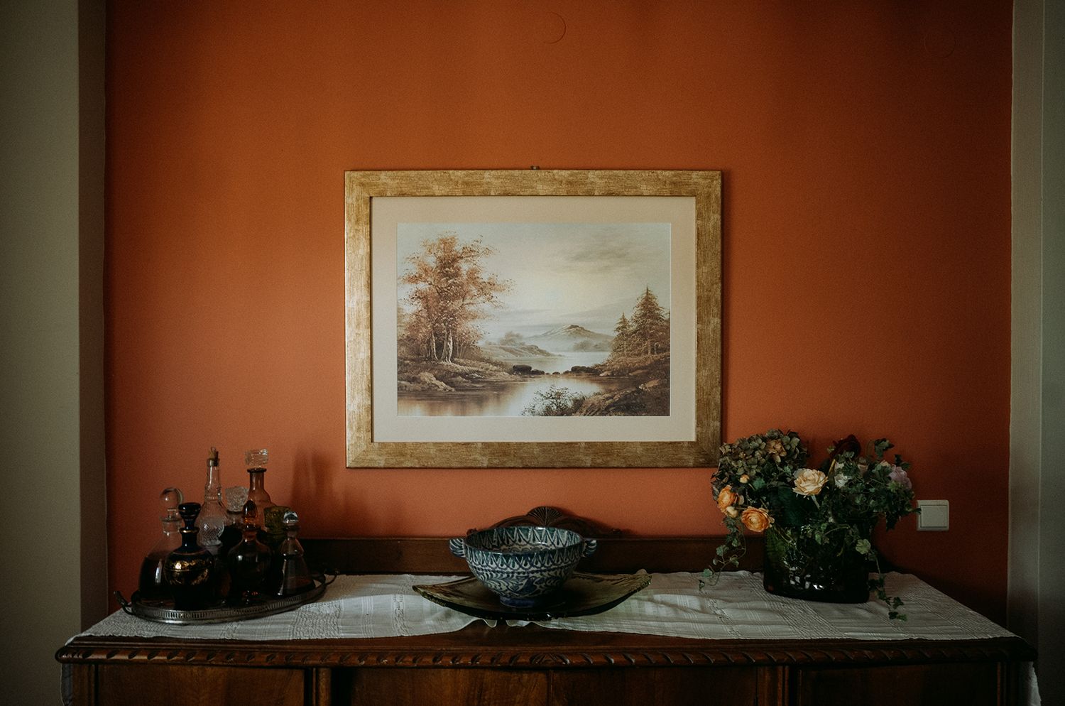 Panoramic view of a rustic interior wall with landscape paintings and vintage decor against a warm terracotta background.