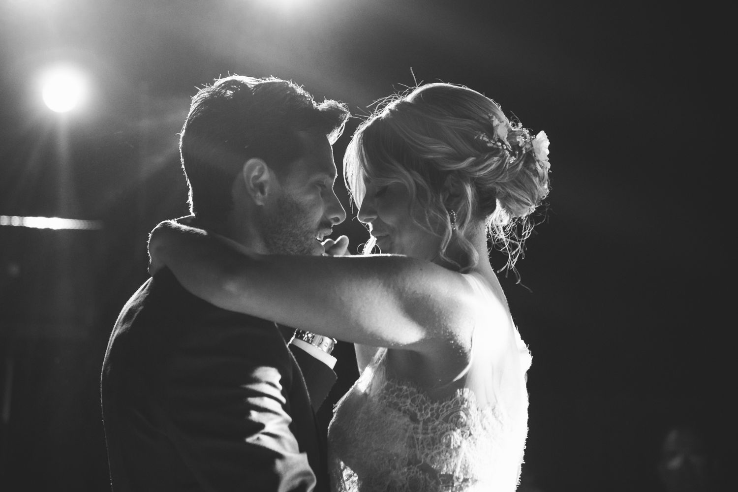 Dramatic black and white wedding dance photo with backlit silhouettes.