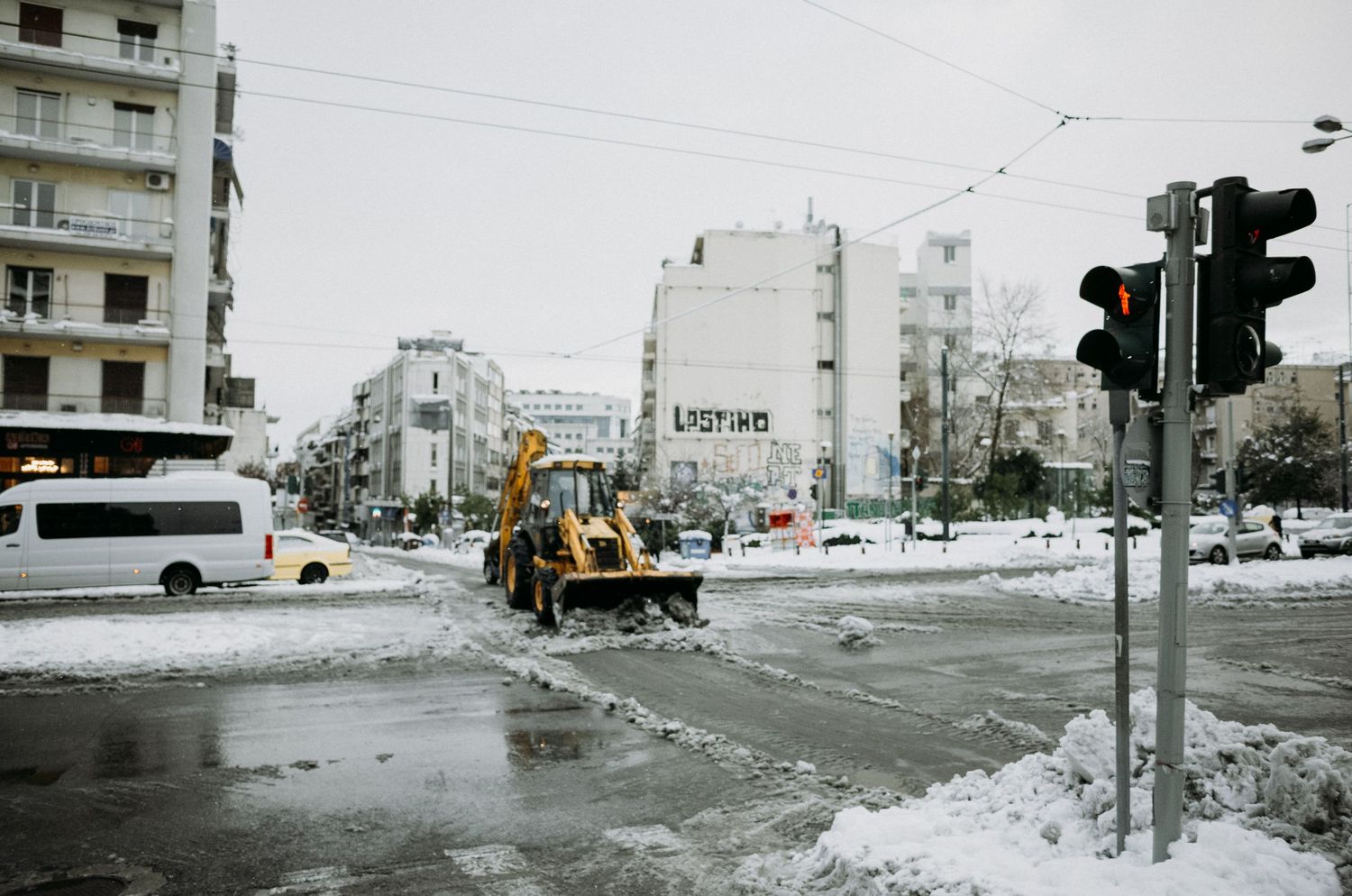 Snowy urban street corner with traffic lights and apartment buildings visible through winter weather conditions.