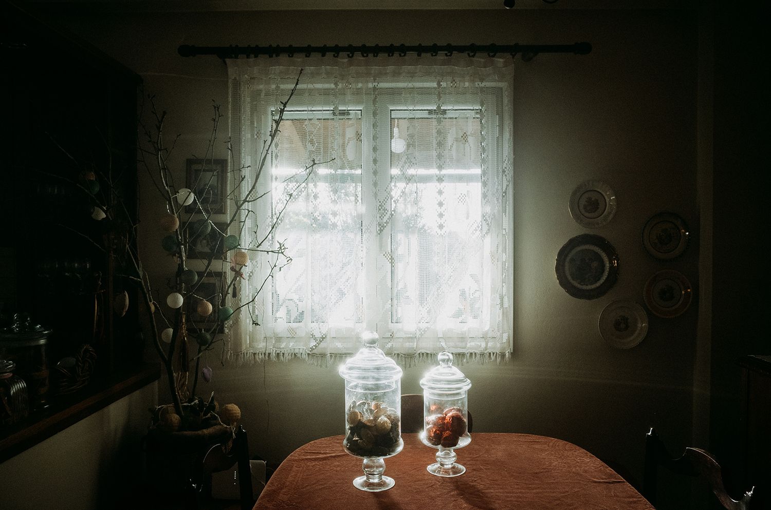 Dark moody interior room with window light casting shadows and glass objects on wooden table.