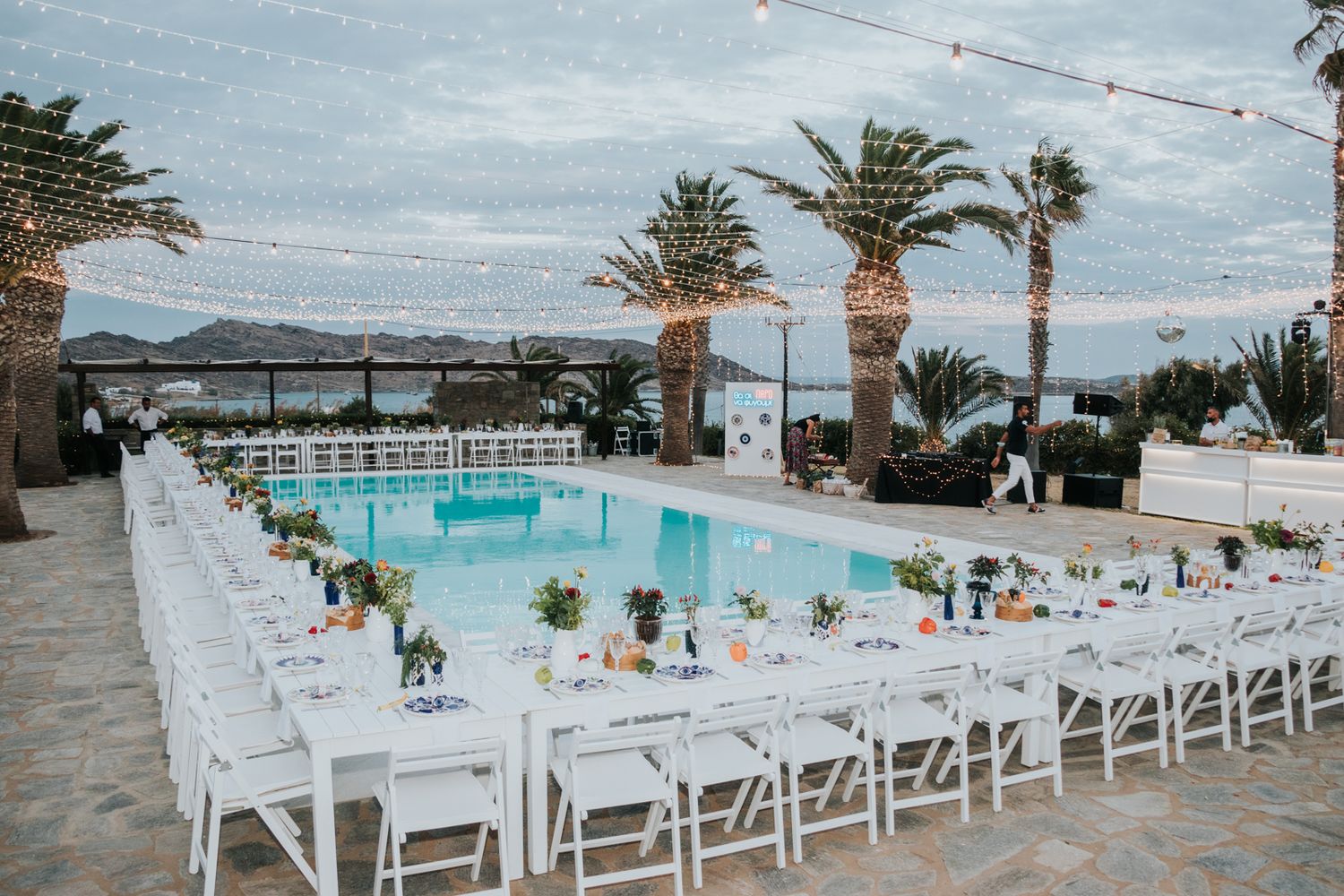 Elegant poolside wedding reception setup with white chairs and palm trees.