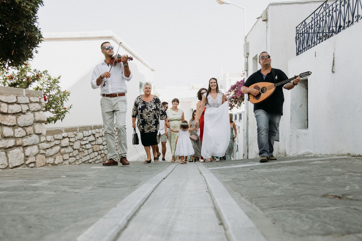 People celebrating at a traditional Greek wedding venue with white stone walls and cobblestone paths.