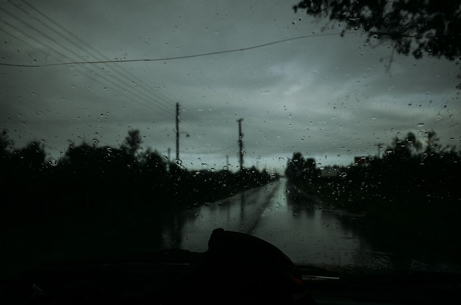 Dark stormy clouds gather over a rural landscape with utility poles and power lines silhouetted against the moody sky.