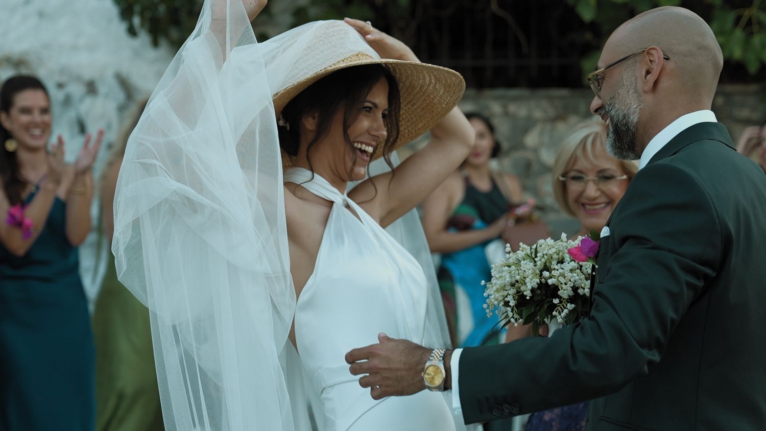 Wedding party celebrates outdoors during a summer garden ceremony with guests and veiled bride.