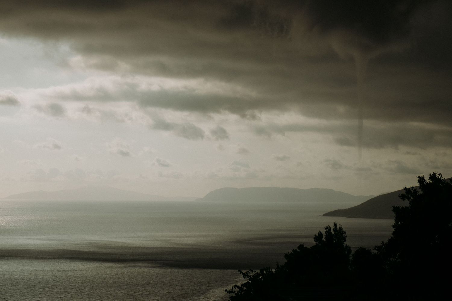 Dark stormy clouds roll over a mountainous landscape at sunset creating a moody atmosphere.