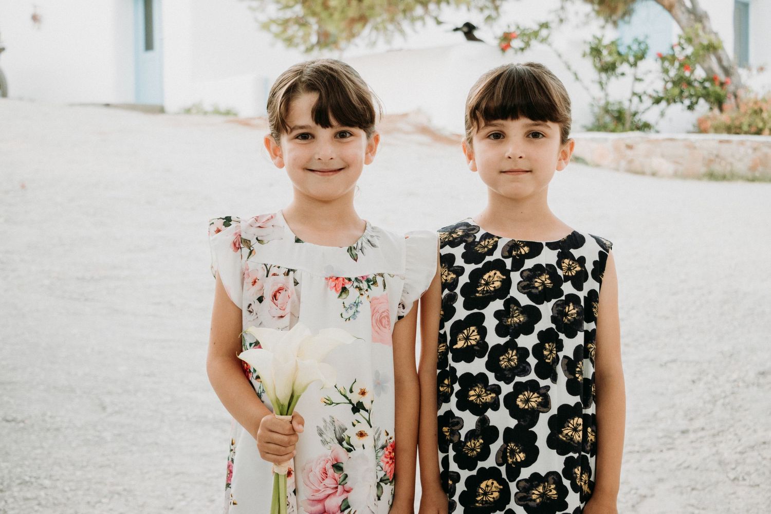 Children in floral and patterned dresses standing together outdoors.