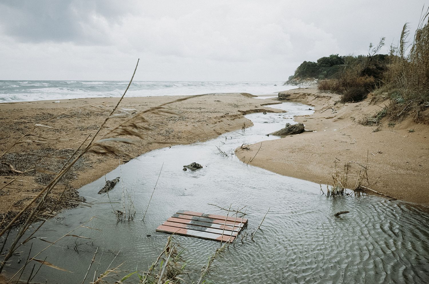 Coastal erosion and flooding along a sandy beach with driftwood and debris scattered on the shoreline.